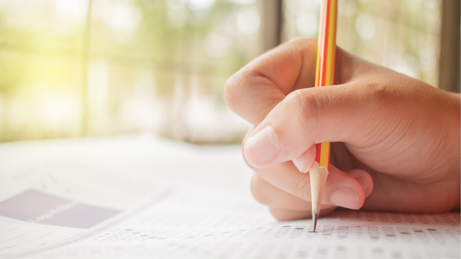 A close-up image of a hand holding a pencil and filling in a circle on a standardized test answer sheet.