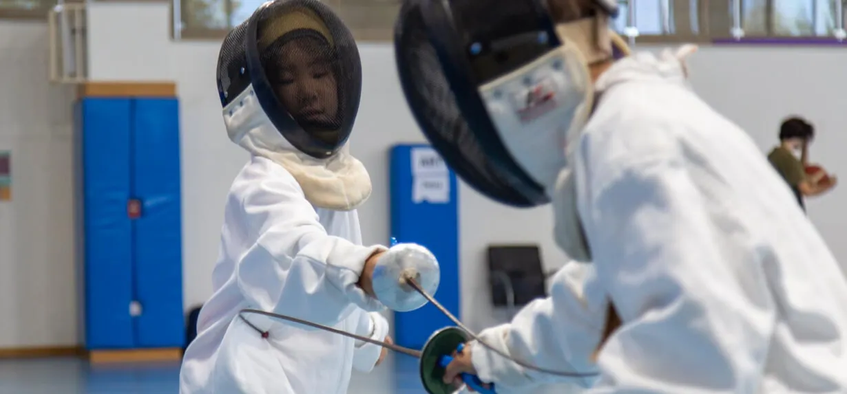 Two King's Academy students engaged in a fencing match.
