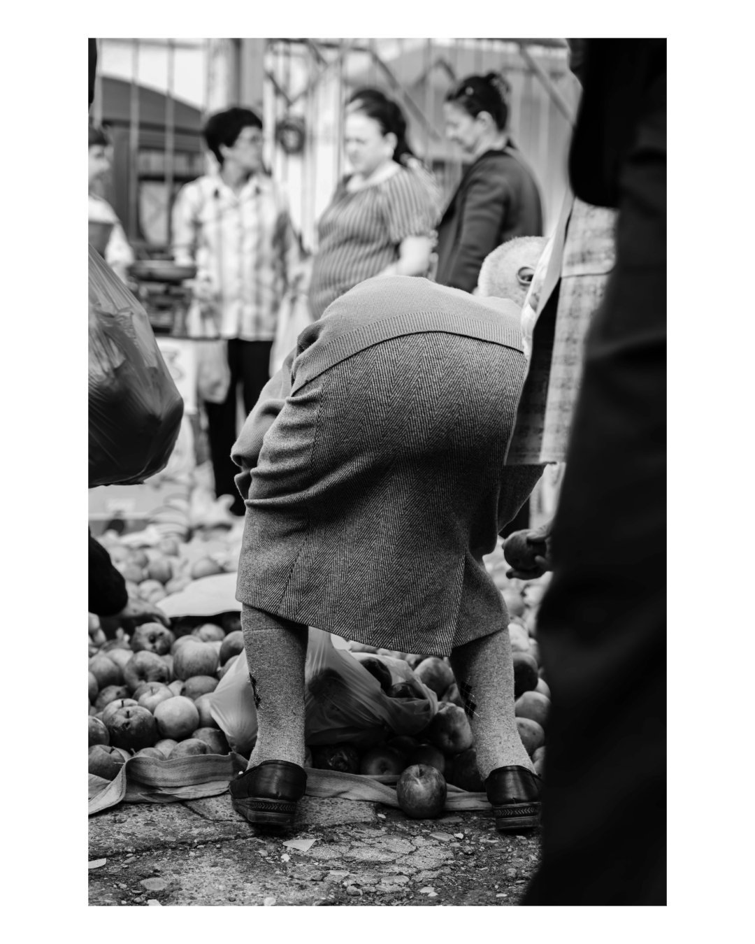 A woman bending over crates of apples at a street market in Albania