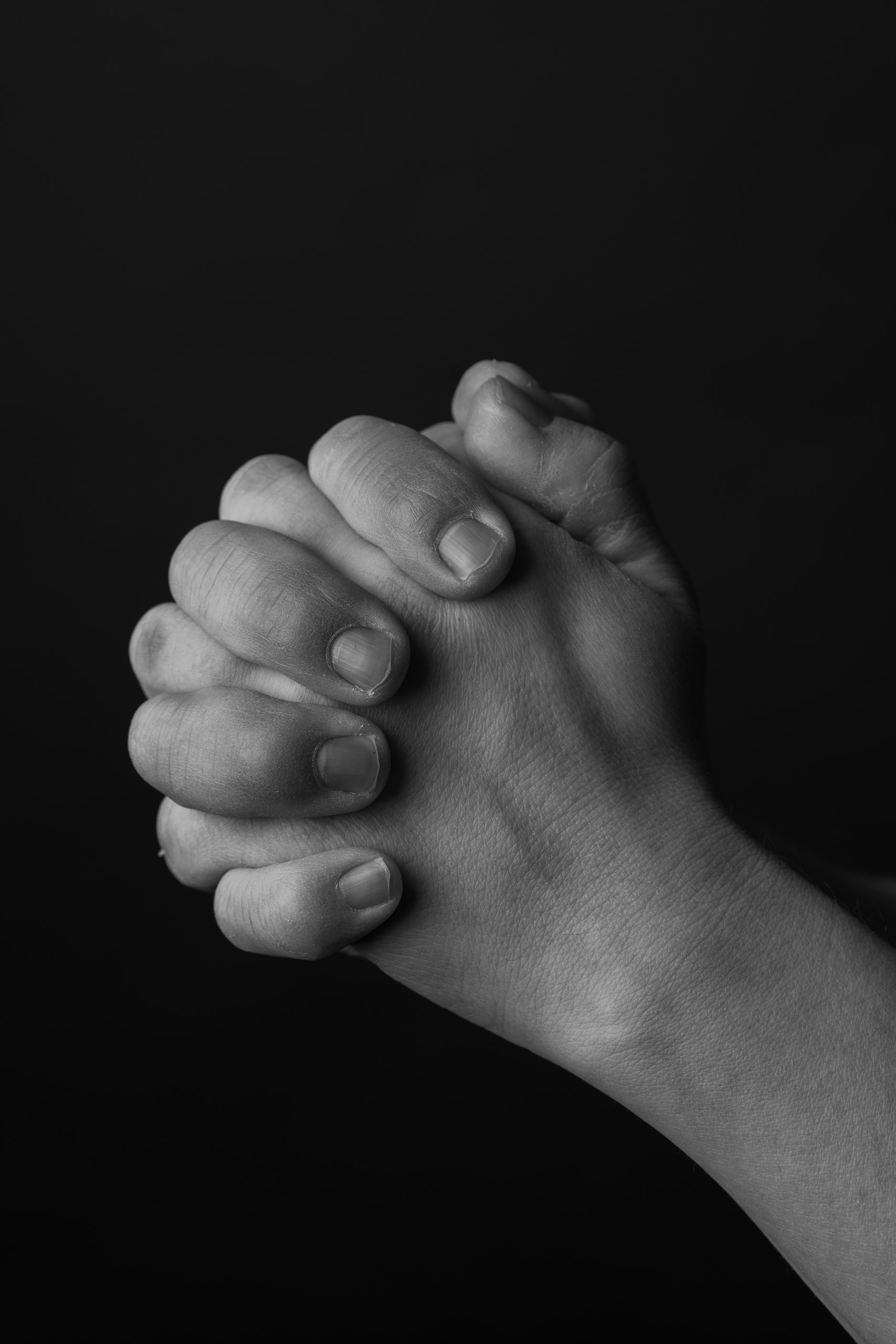 Two hands clasped together against a black background