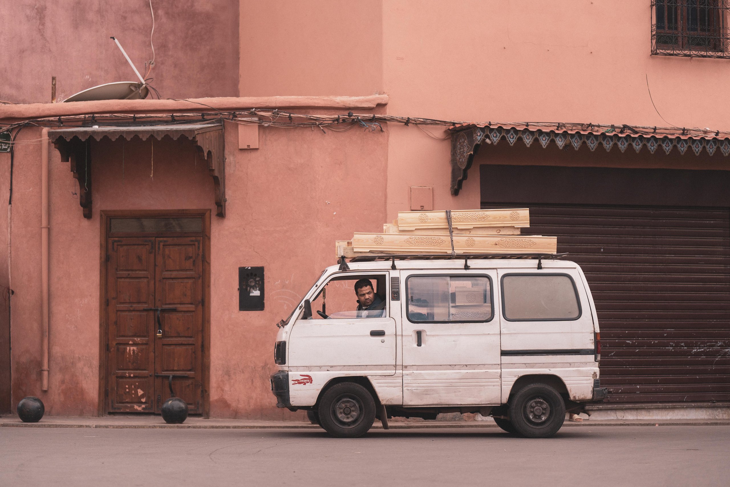 A white van loaded with carved wooden panels in a pink street of Marrakech