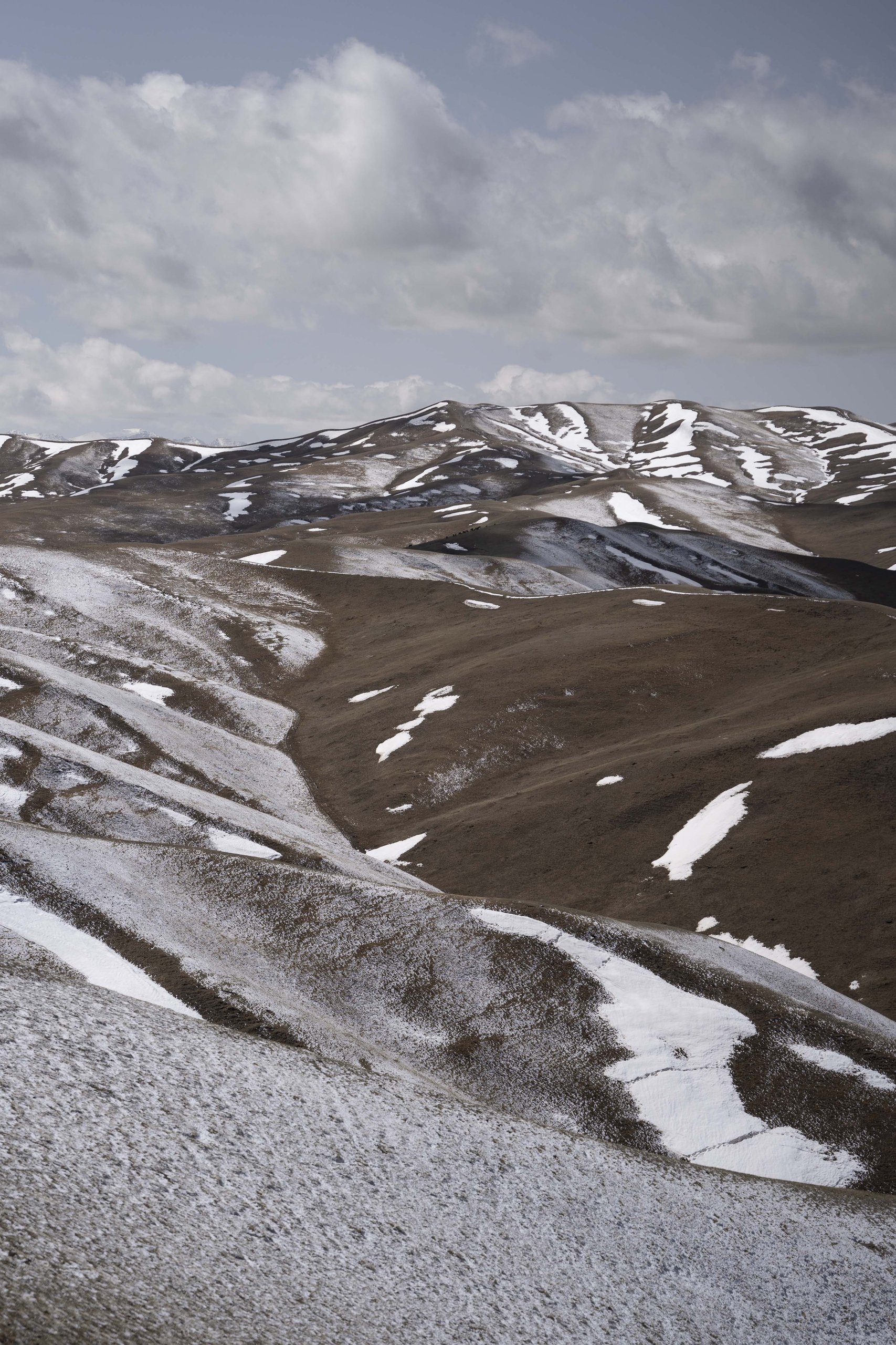 Layered hills with streaks of snow under a clouded sky