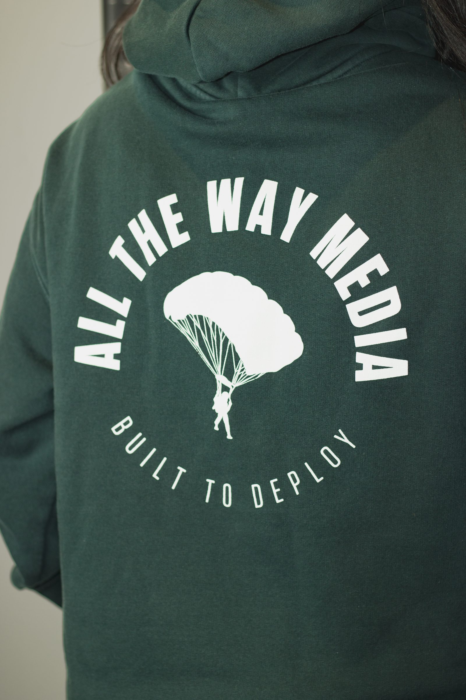 The All the Way Media parachute logo on a green hoodie.