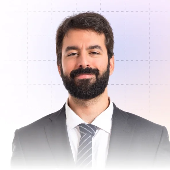 Portrait of a smiling man with dark hair and beard wearing a suit, white shirt, and striped tie against a light background.