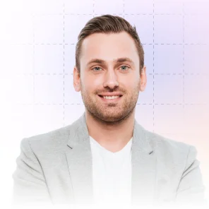 Smiling man with short brown hair wearing a light gray blazer and white shirt against a light background.