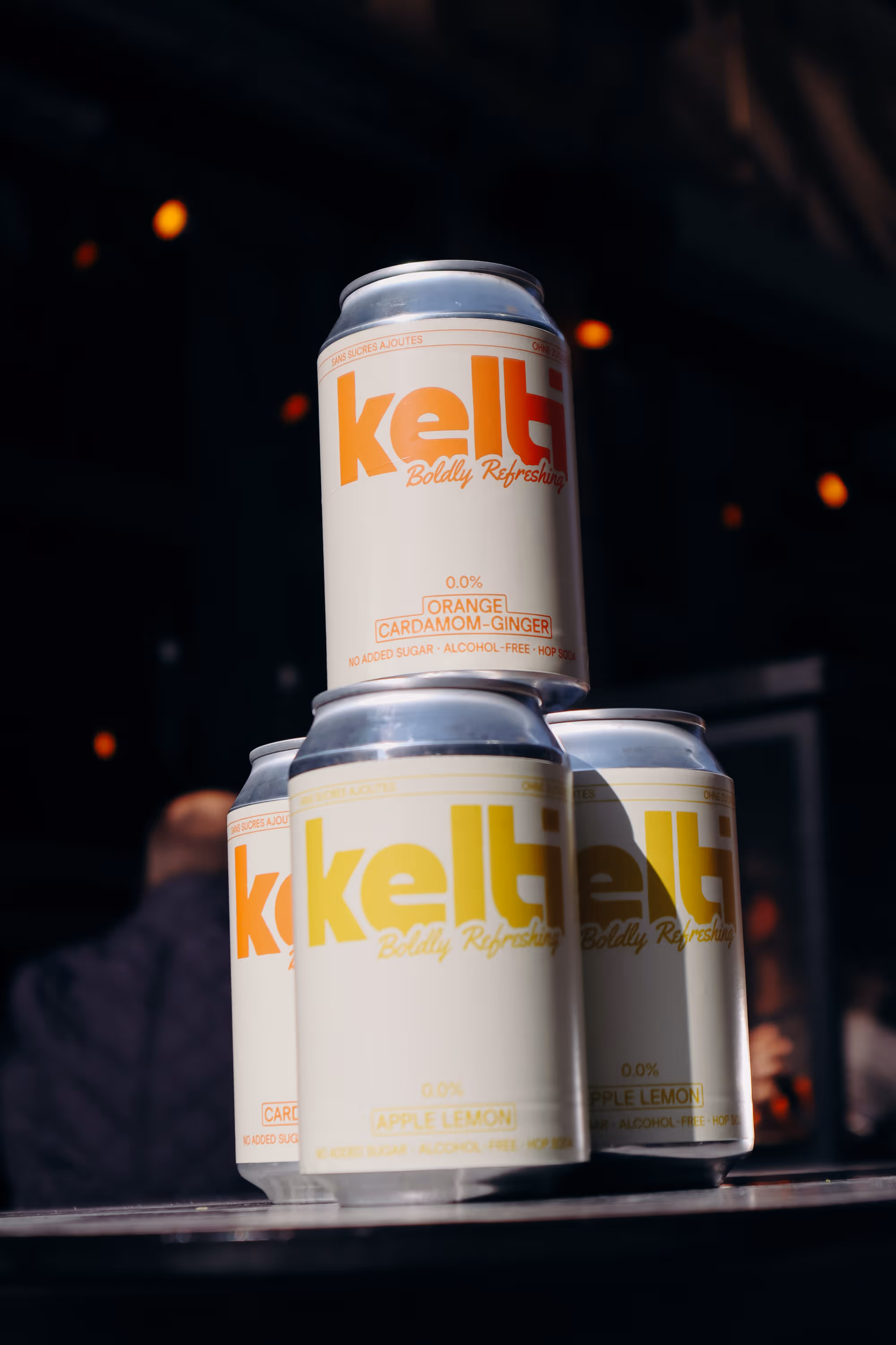 Stack of Kelt cans with flavors orange cardamom-ginger and apple lemon in dark background.