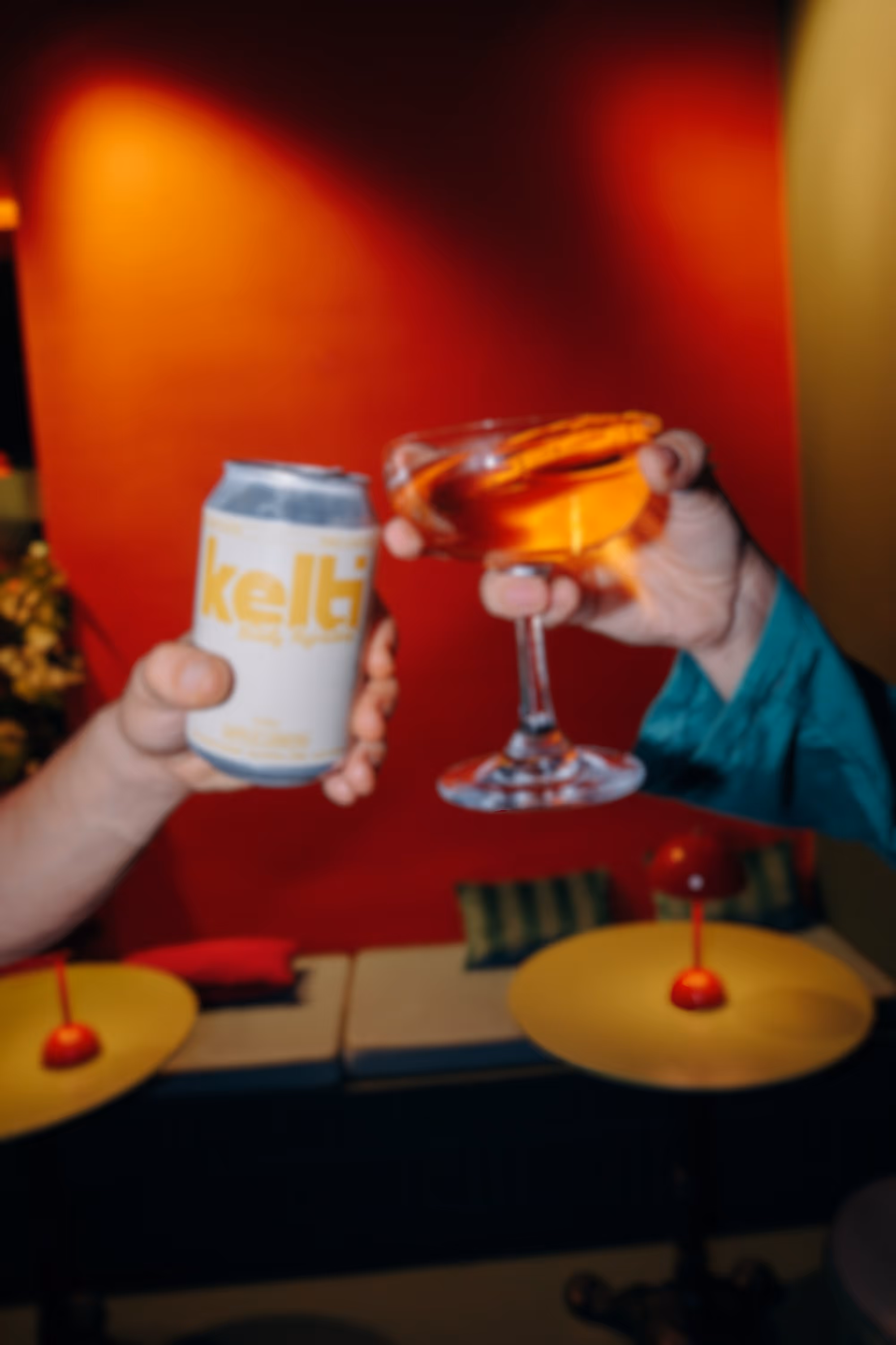 Two people toasting drinks: one with a can and the other with a cocktail glass.