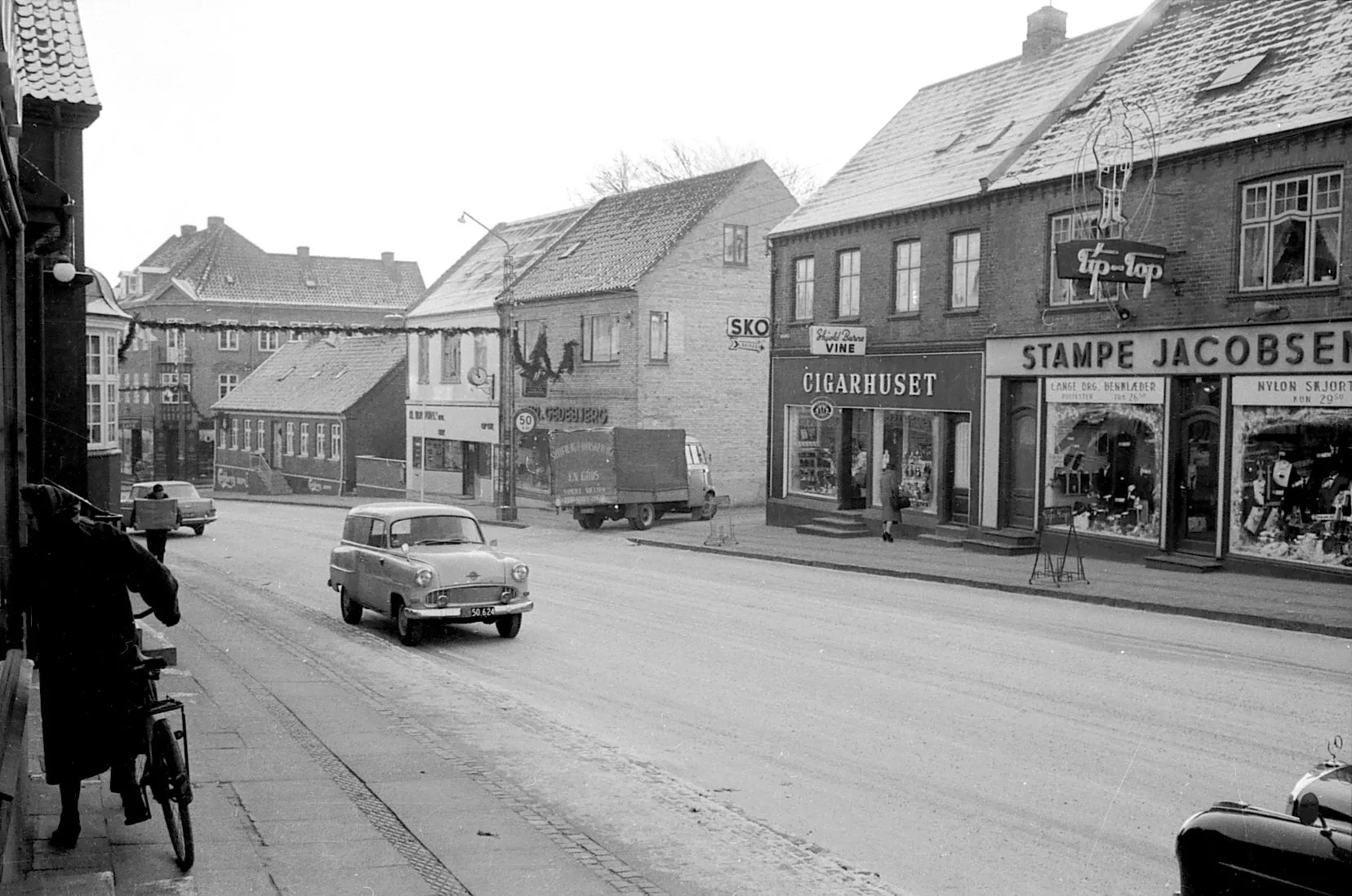 Sort-hvidt gadebillede fra Aars omkring 1960 med Cigarhuset, Stampe Jacobsen og en bil på hovedgaden