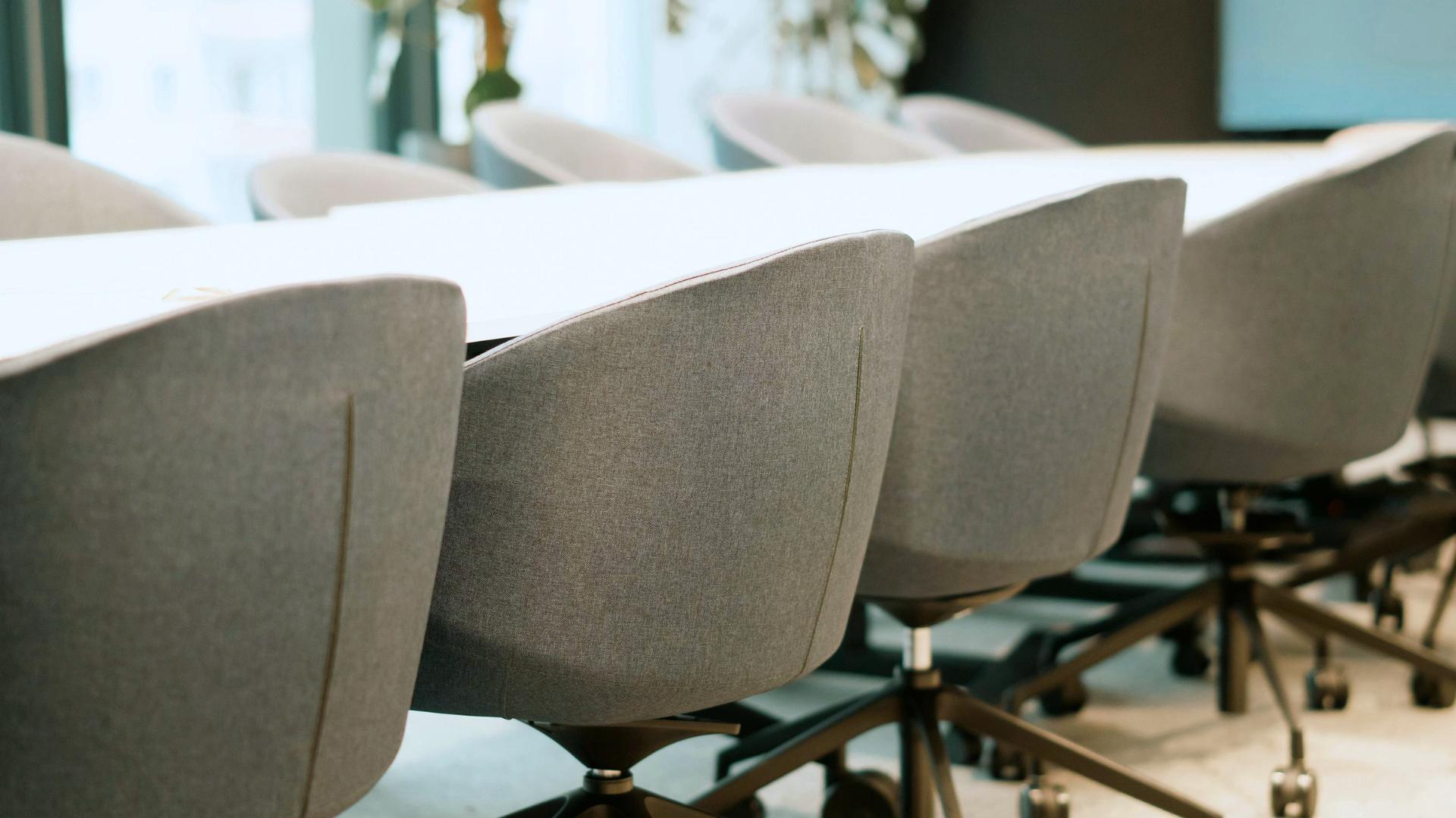 Close-up of gray office chairs with wheels lined up along a white conference table.
