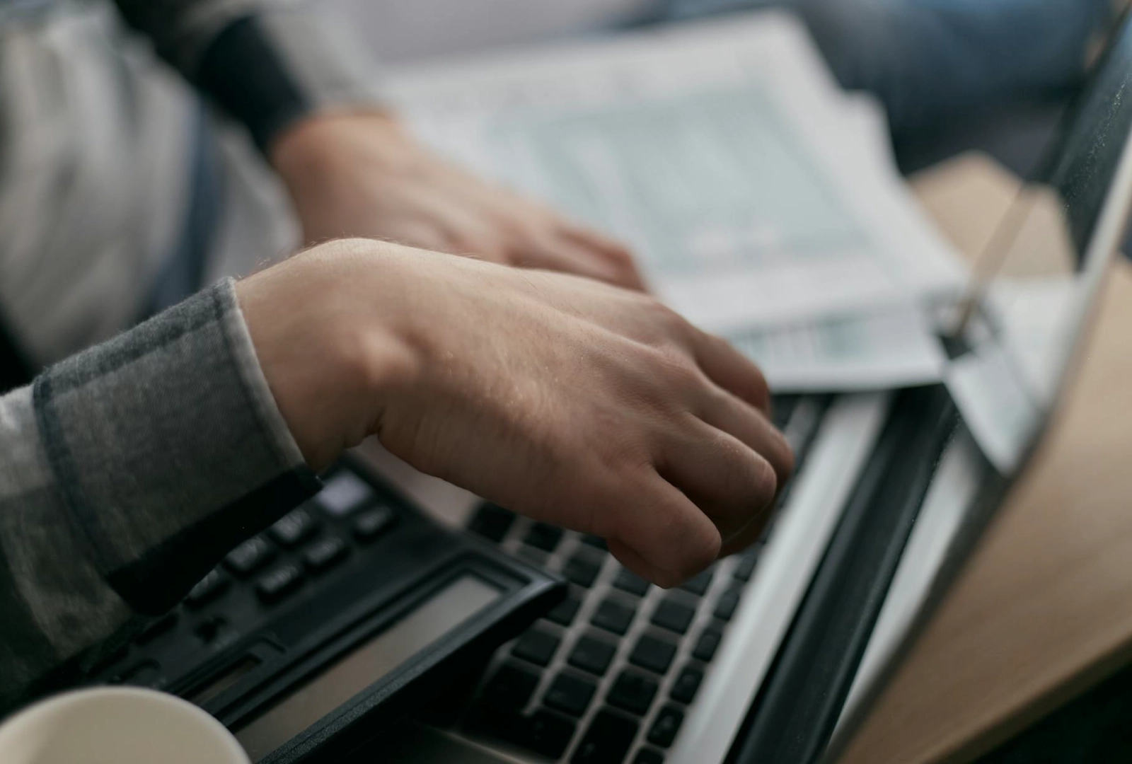 Hands typing on a laptop with financial documents