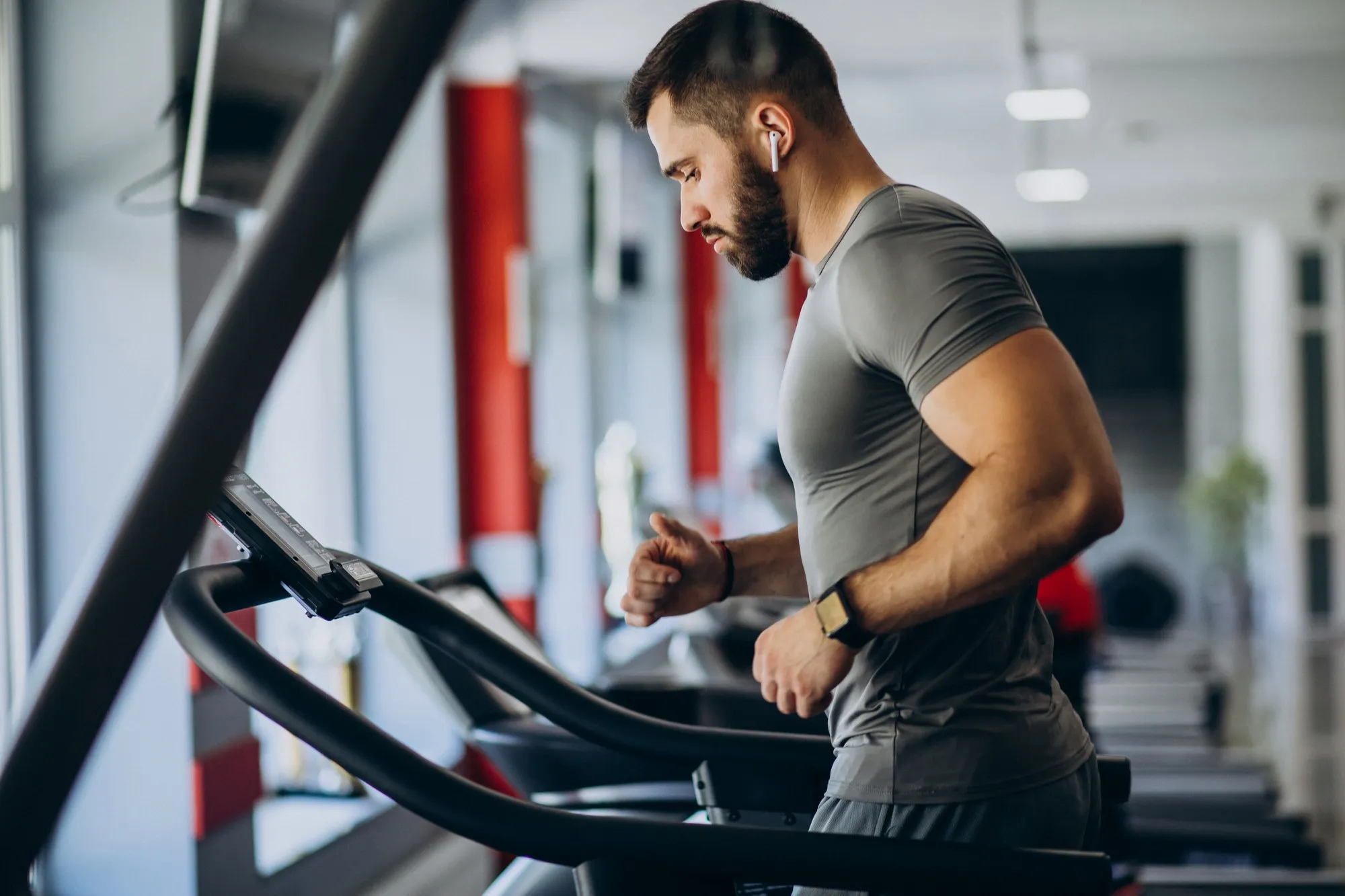 Man wearing earbuds and smartwatch running on a treadmill inside a gym.