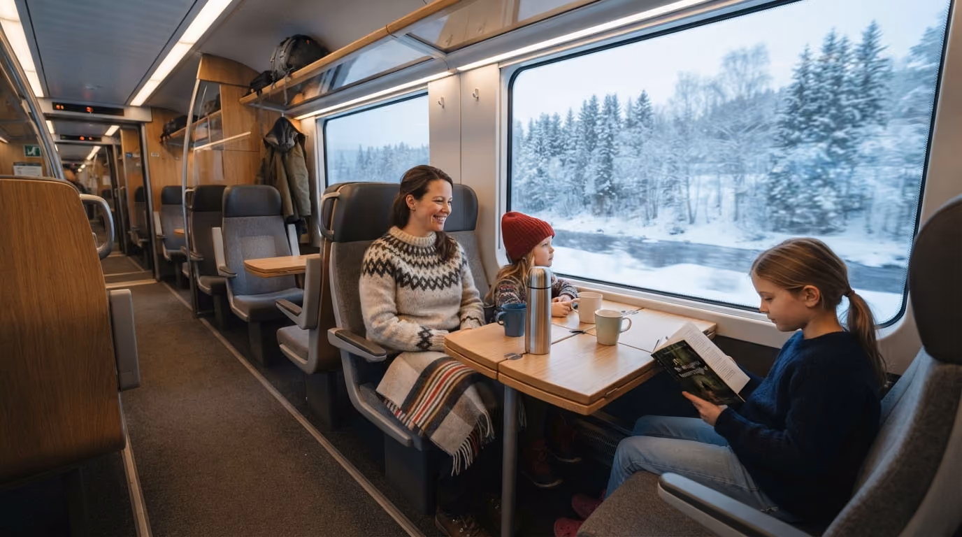 Woman and two girls seated around table inside train with snowy forest scenery outside window.