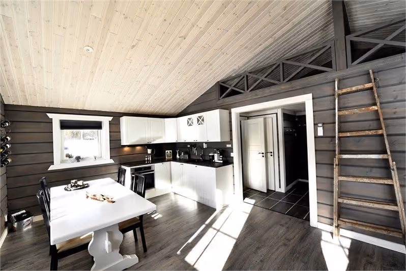 Bright kitchen with white cabinets, black countertops, a dining table, wooden walls, and a rustic ladder.