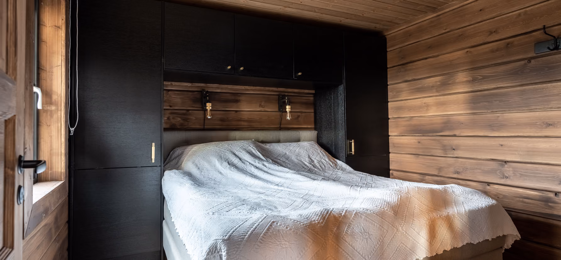 Cozy bedroom with white textured bedspread, black built-in cabinets, and wood-paneled walls and ceiling.
