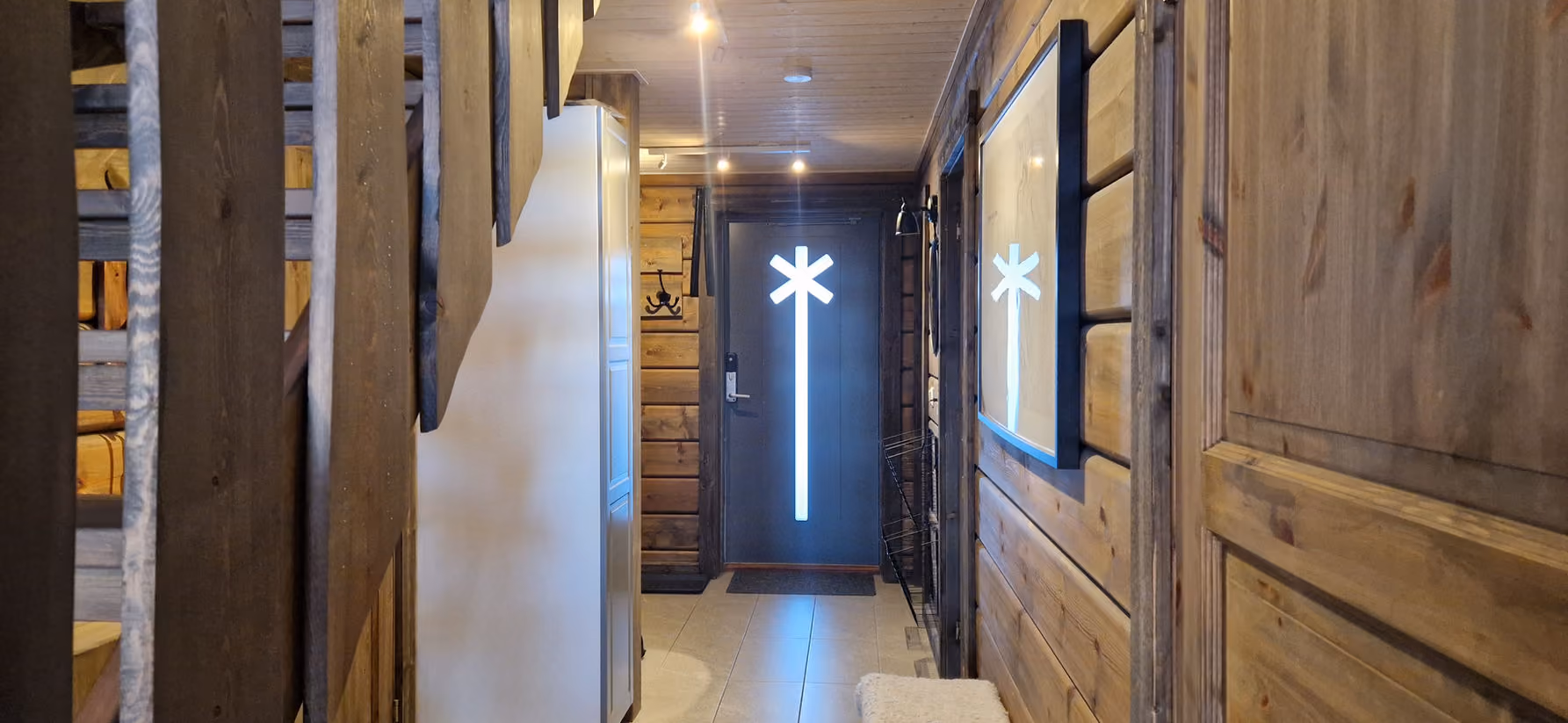 Hallway with wooden walls and ceiling leading to a dark door with a vertical lit asterisk design.