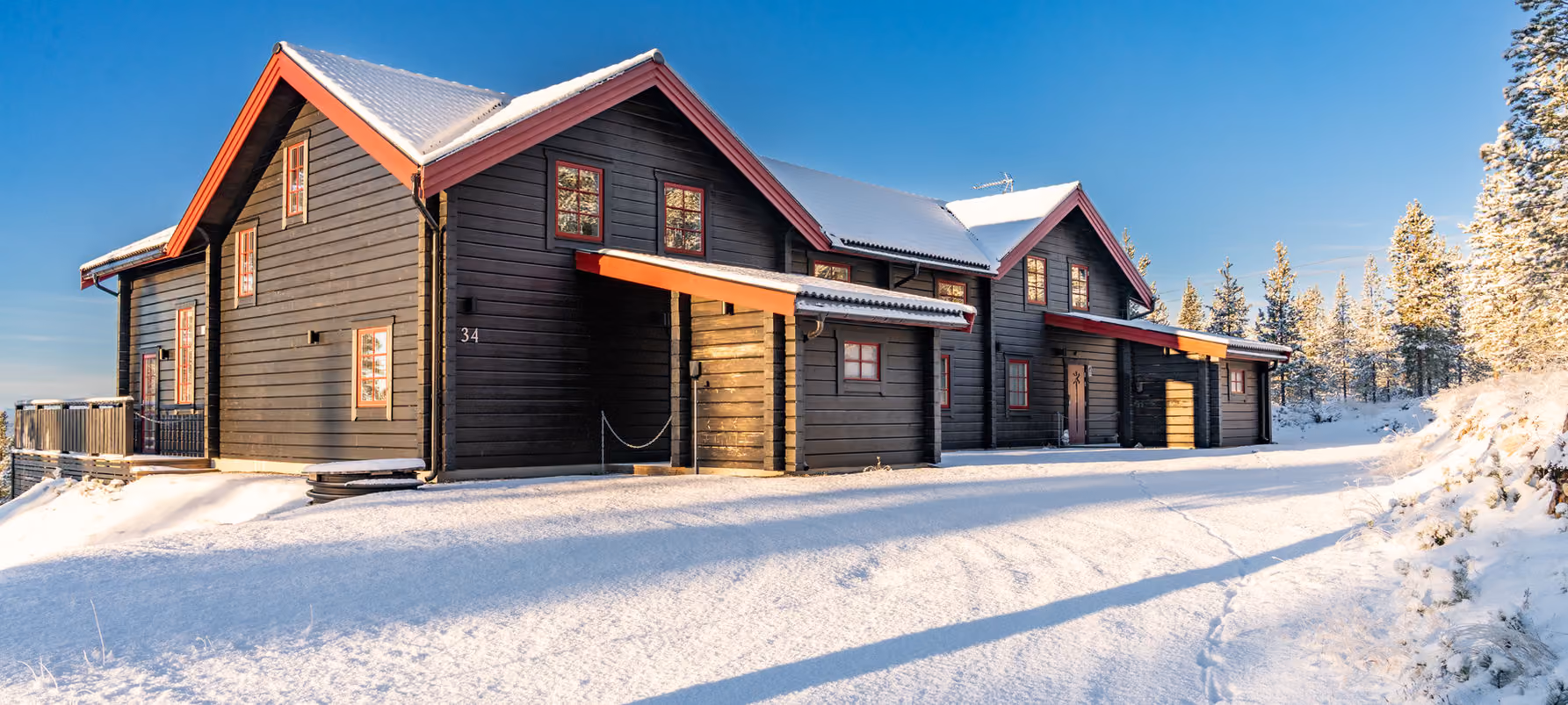 Large black cabin with red-trimmed windows in snowy landscape under clear blue sky.