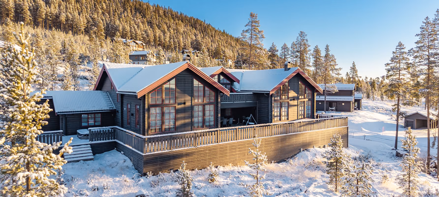 Snow-covered wooden lodge surrounded by pine trees under a clear blue sky in a winter landscape.