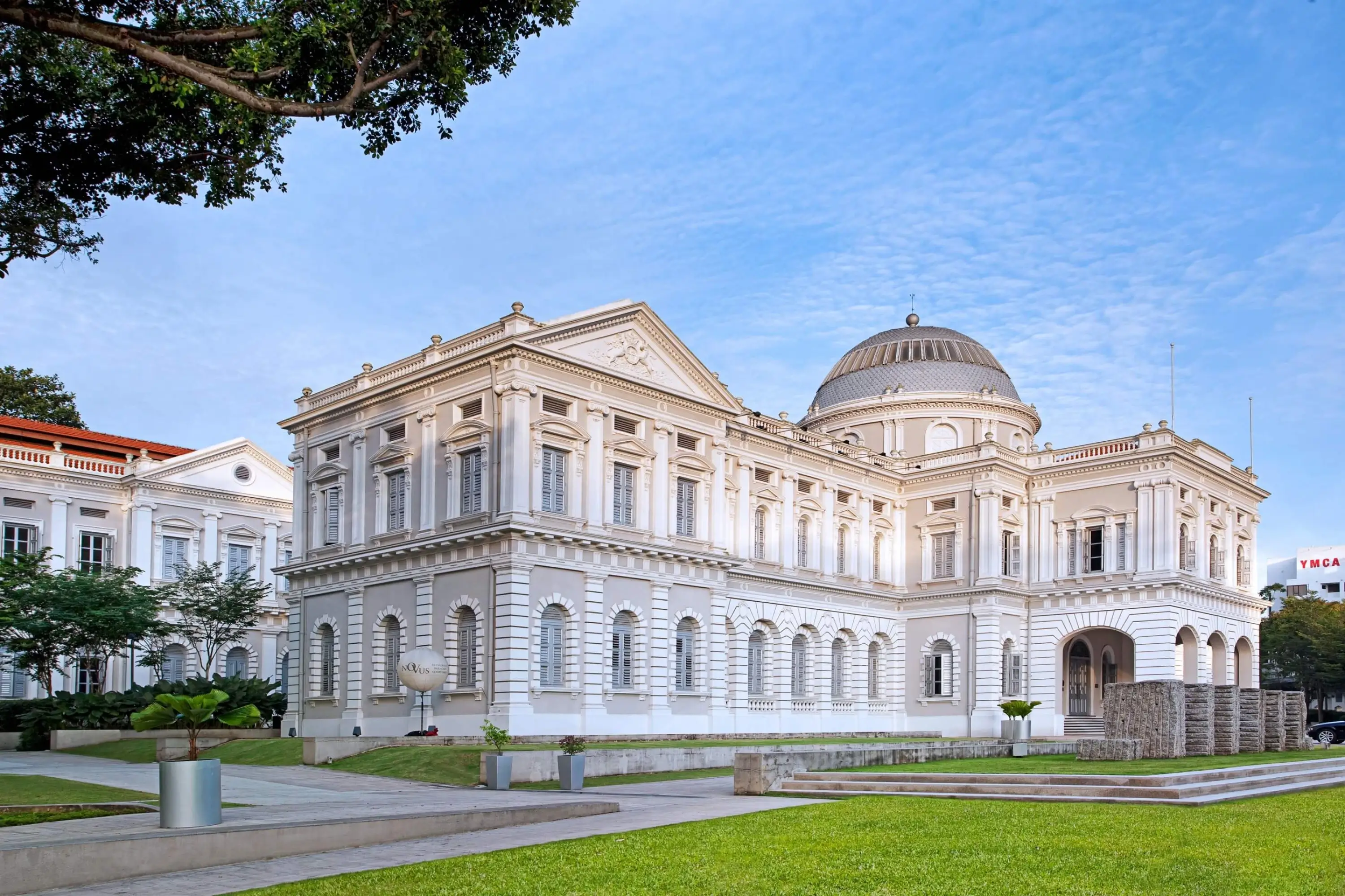 The neoclassical facade of the National Museum of Singapore bathed in morning light, its domed rotunda rising against a blue sky.