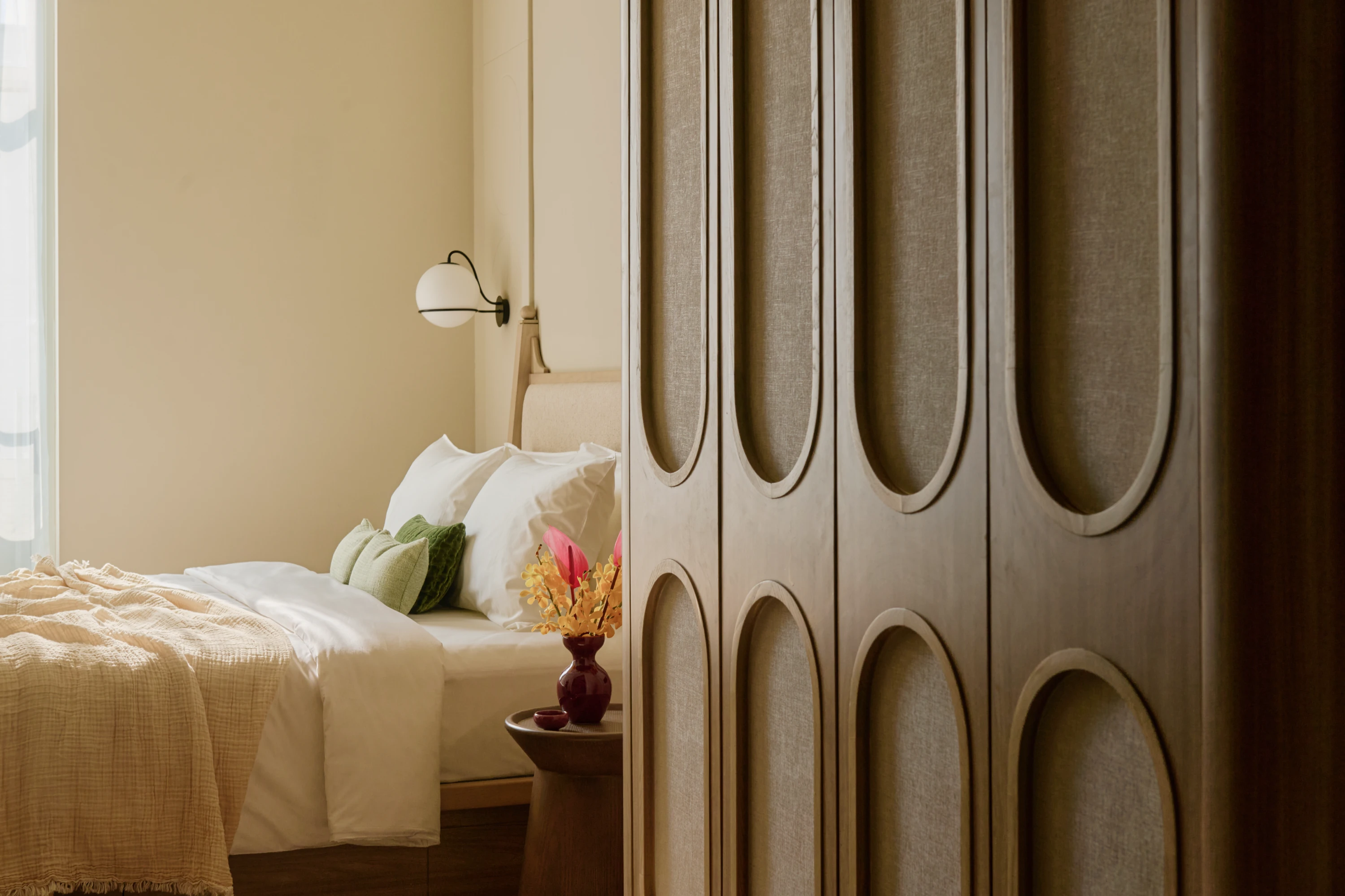 The Deluxe apartment's oval-panelled wardrobe in the foreground, framing a glimpse of the bed dressed in white linen and green cushions beyond.