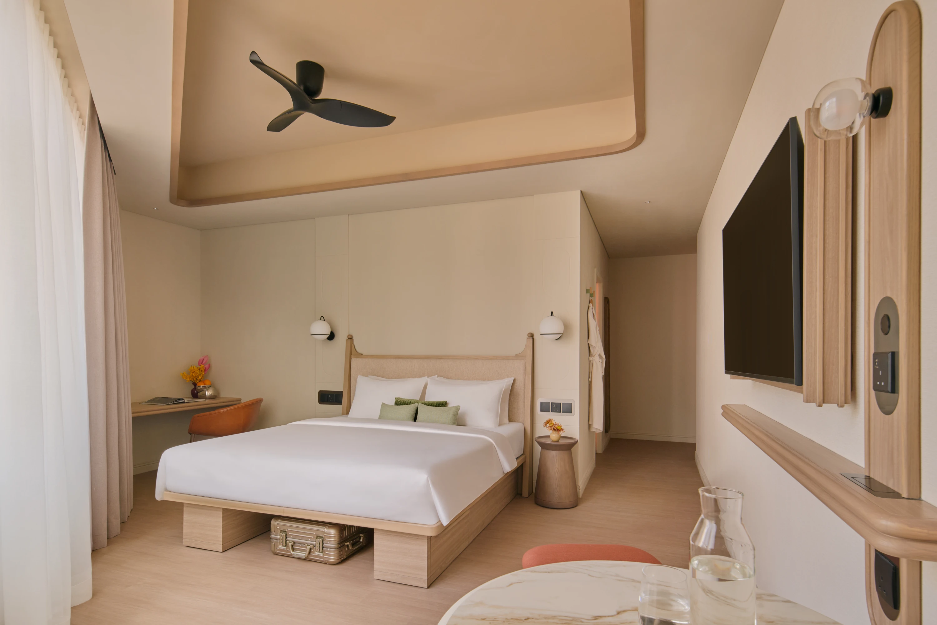 The Urban apartment bedroom with a platform bed, globe wall sconces, a desk nook with a terracotta chair, and a gold suitcase tucked beneath the bed frame.