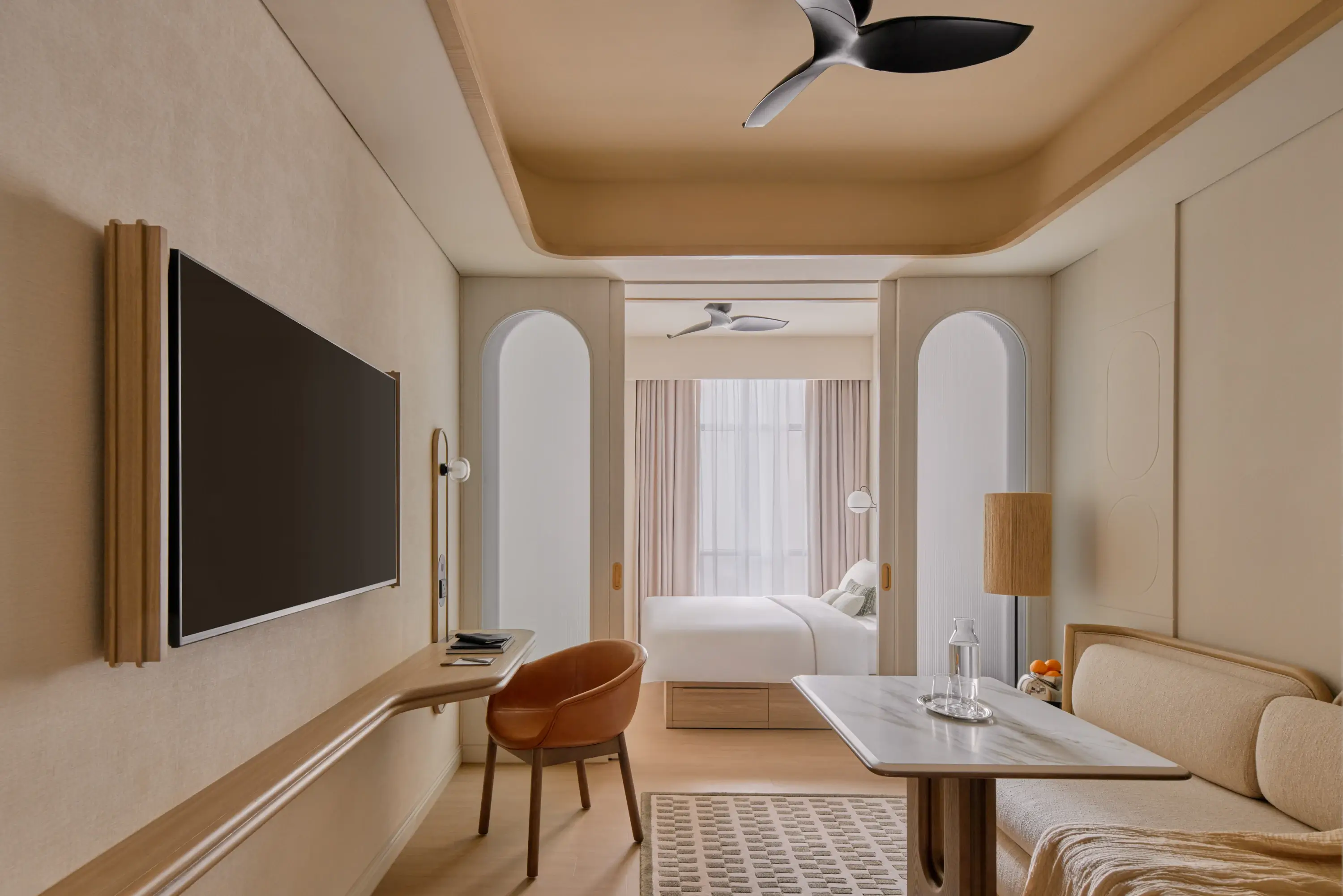 The Stamford Suite living area with a terracotta chair at the desk, a marble side table, and arched doorways framing the bedroom and its pink curtains beyond.