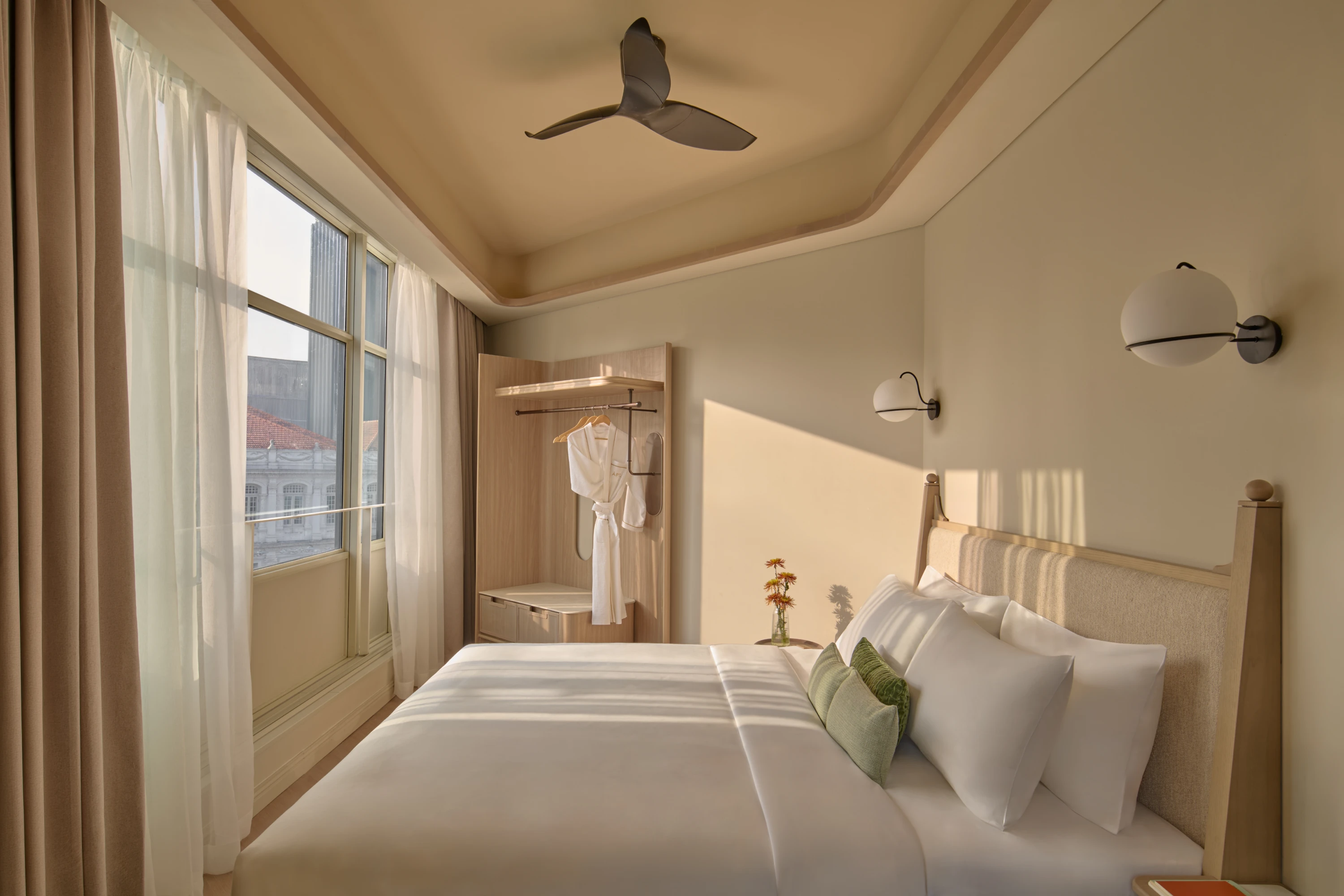 The Civic Suite bedroom bathed in warm morning light, a bathrobe hanging in the open wardrobe beside floor-to-ceiling windows overlooking the city.