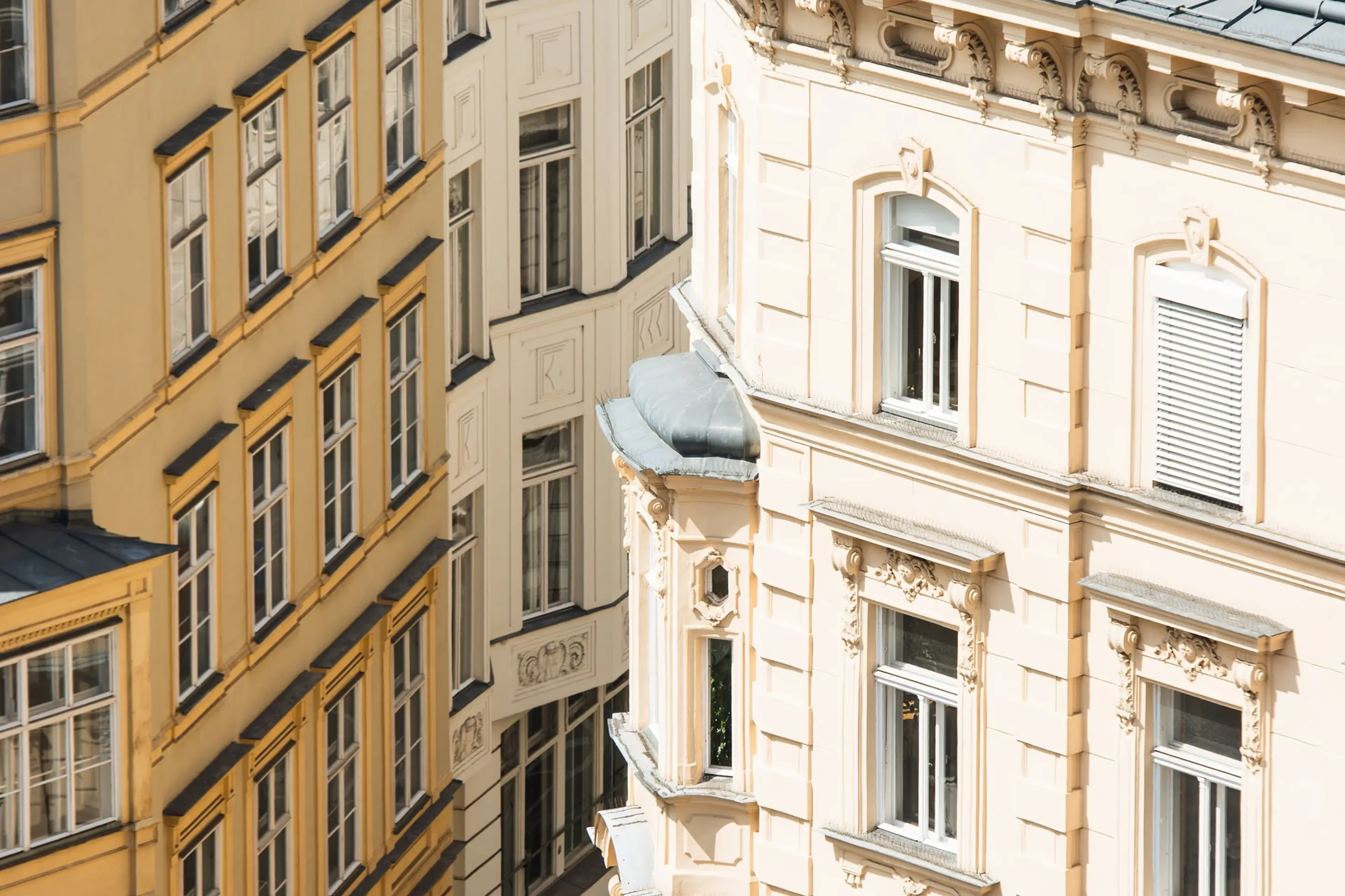 Nahaufnahme verzierter Wiener Altbau-Fassaden in Gelb und Creme mit Erkern und dekorativen Steinverzierungen im warmen Sonnenlicht.