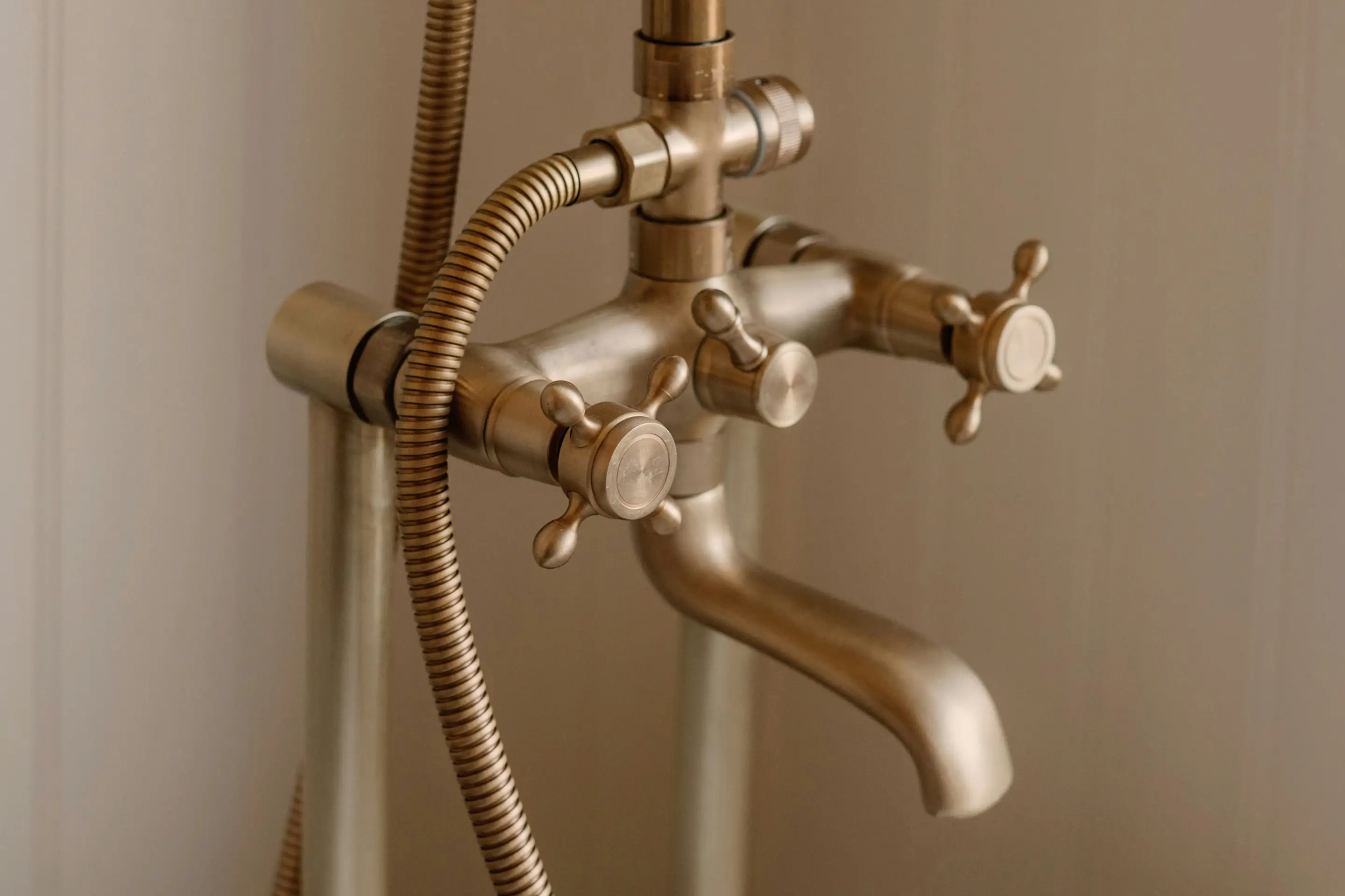 Klassische Wasserarmatur aus Messing mit Kreuzgriffen und Brauseschlauch als Sinnbild für sicheres Warmwasser in Gebäuden
