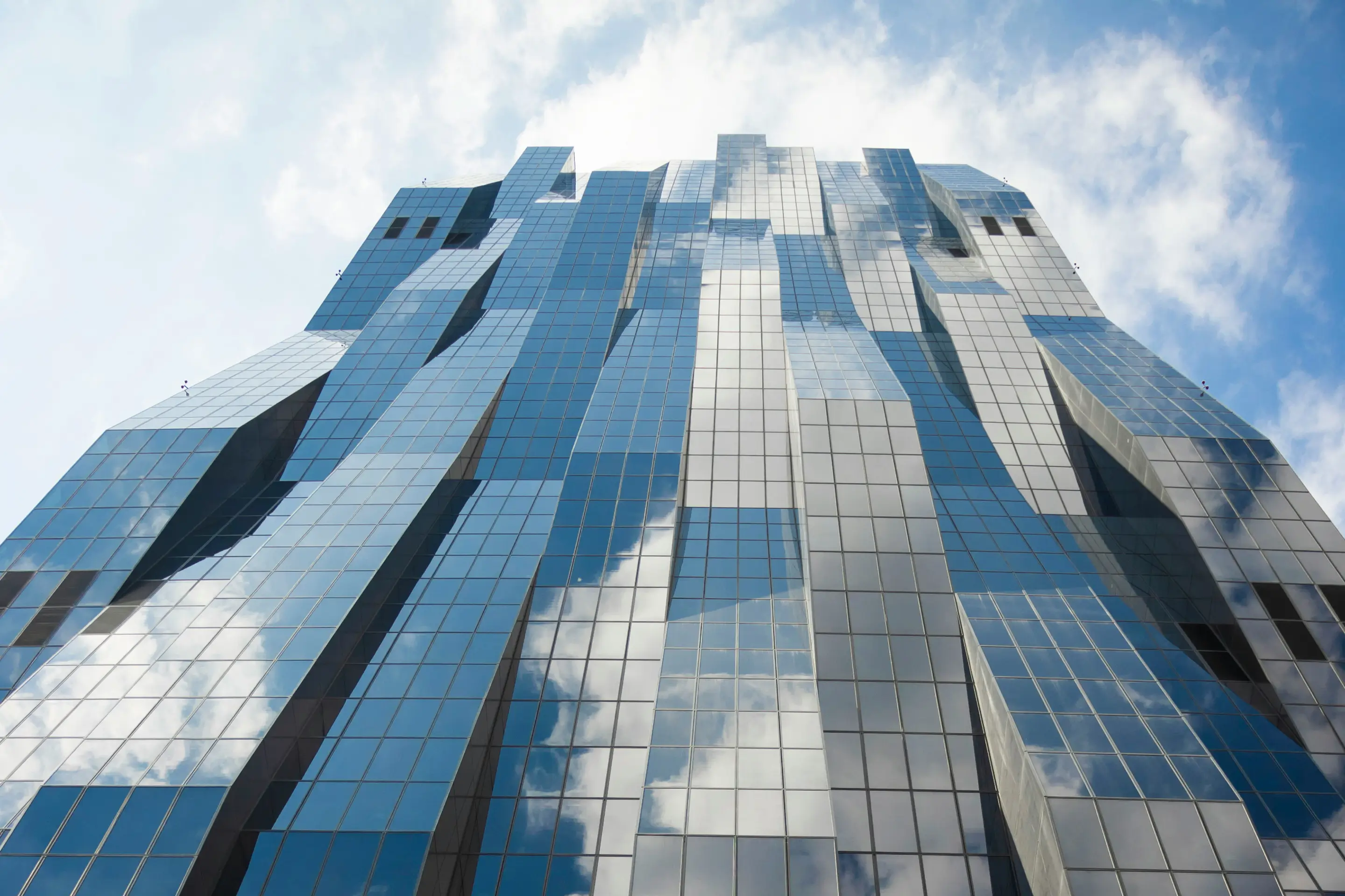Modernes Bürohochhaus mit verspiegelter Glasfassade, in der sich der bewölkte Himmel spiegelt, als Sinnbild für Büro- und Gewerbeimmobilien