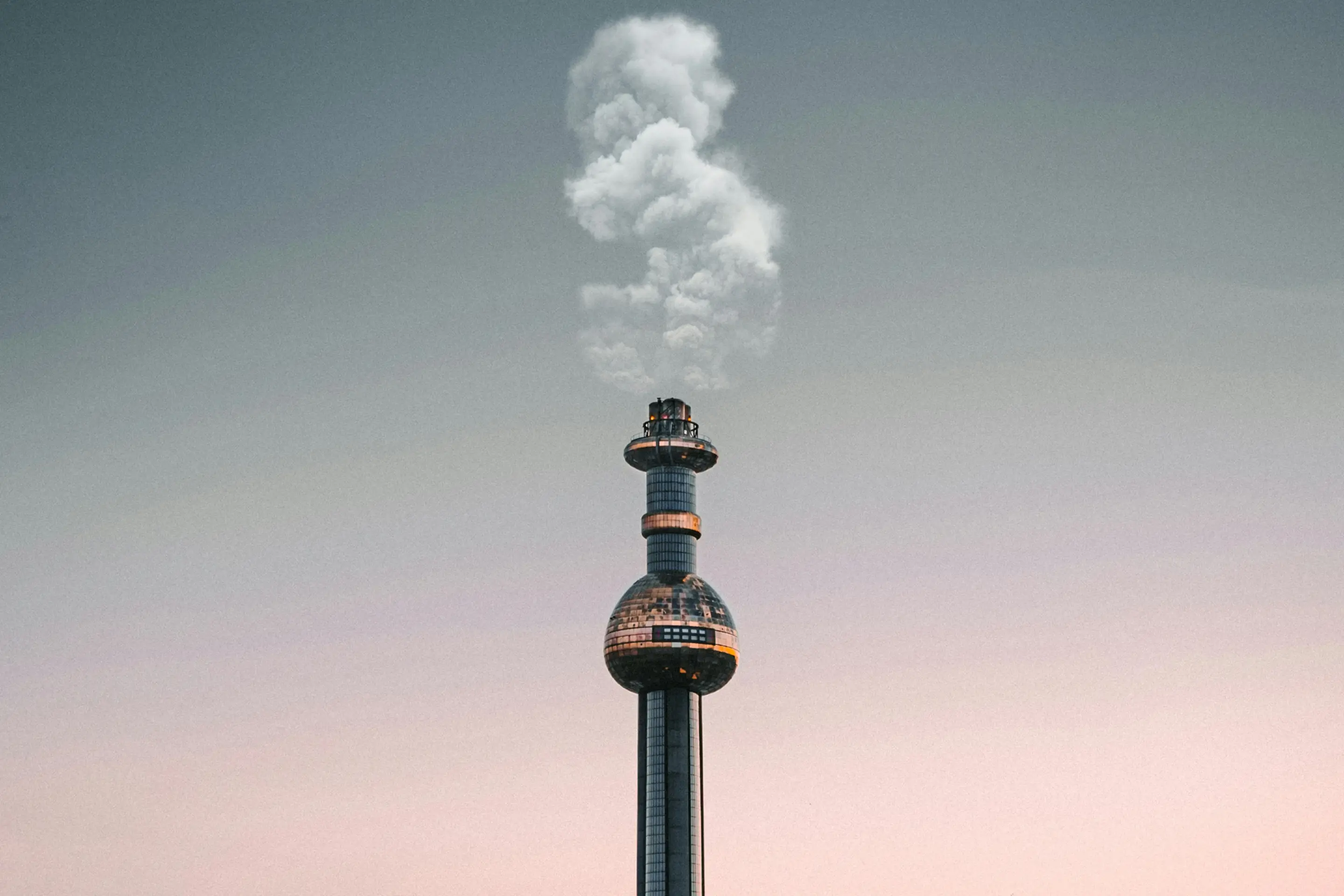 Hoher Industrieschornstein mit aufsteigender Dampffahne vor dämmrigem Himmel als Sinnbild für Industrieanlagen