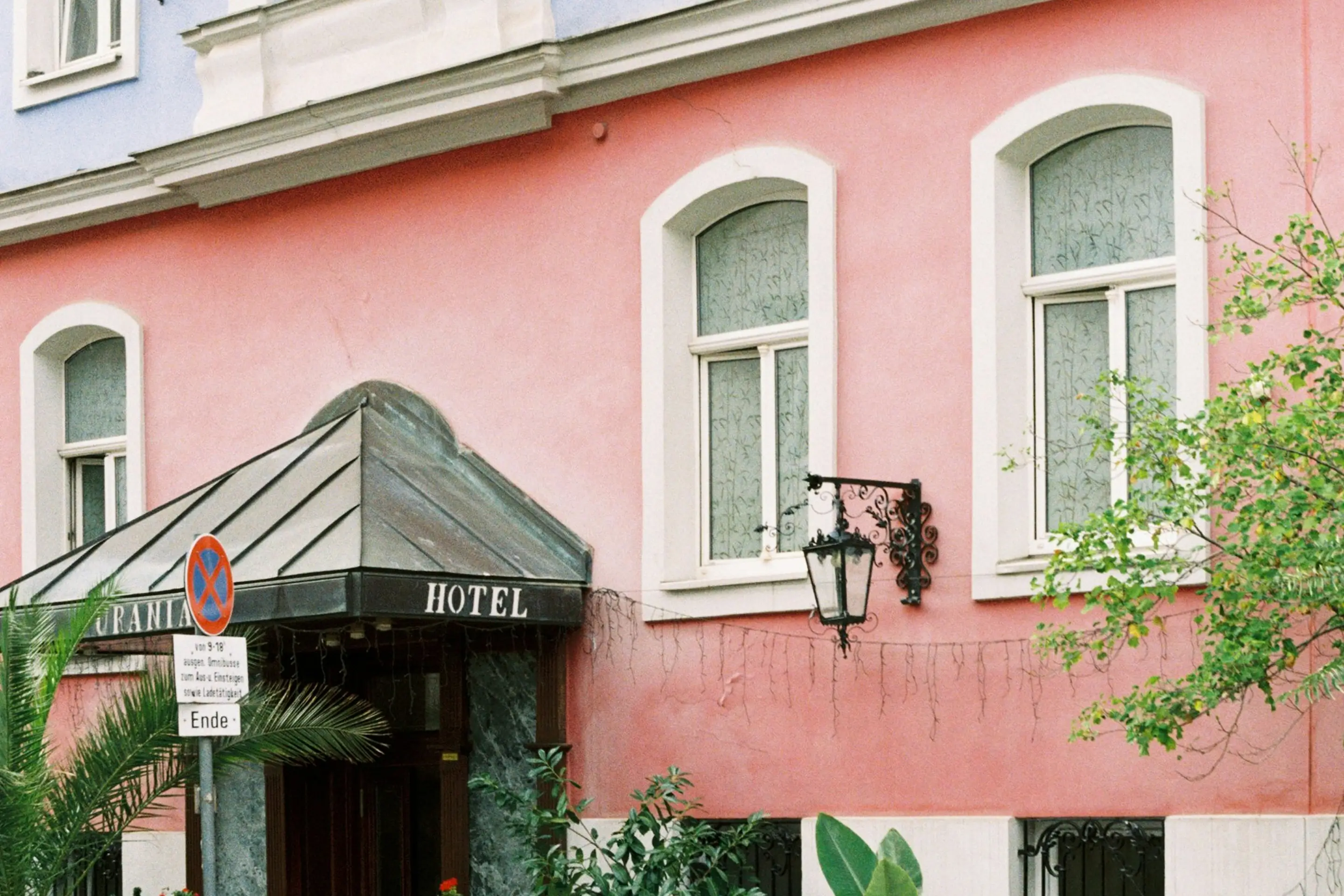 Rosa Altbaufassade eines Hotels mit Vordach, Rundbogenfenstern und schmiedeeiserner Laterne als Sinnbild für Hotels und Gastgewerbe