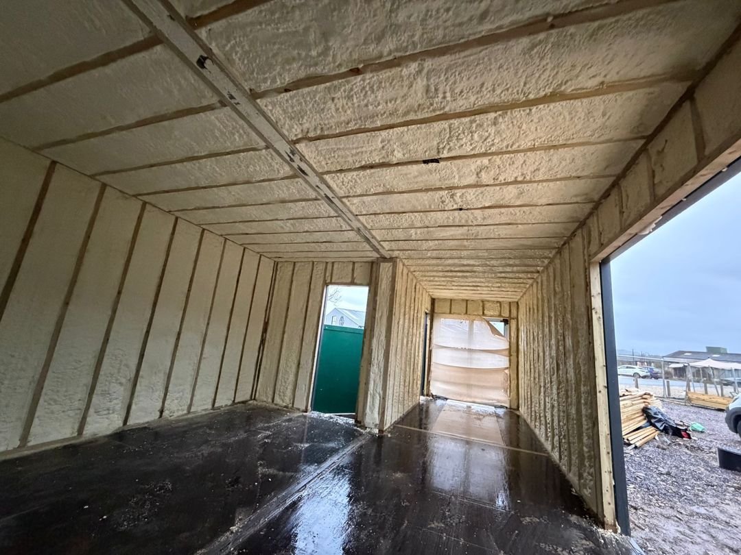 A container interior with walls and ceiling insulated with closed-cell spray foam between timber battens, ready for lining.