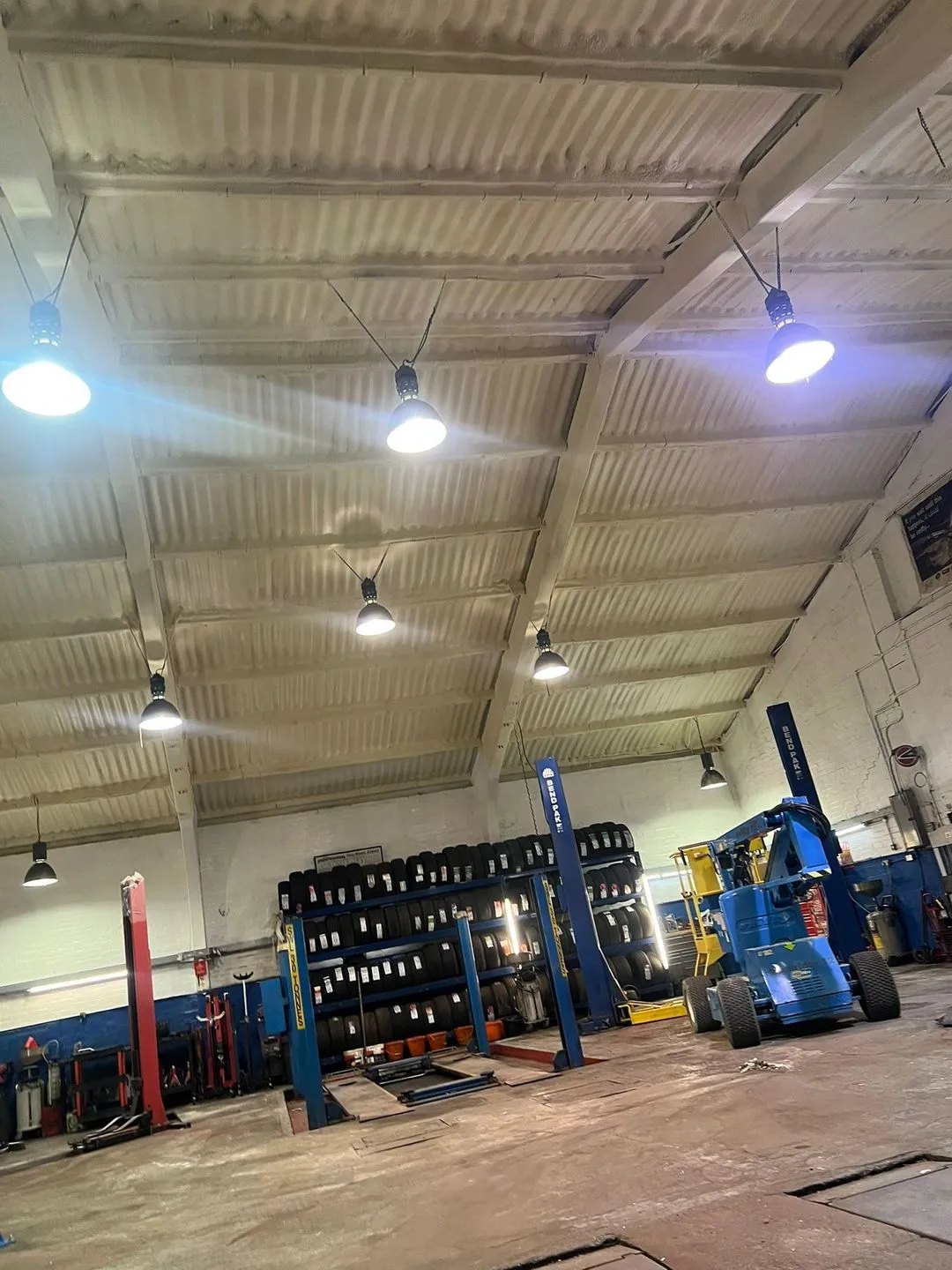 An MOT bay with its roof and upper walls sprayed in a cream closed-cell layer, vehicle lift and inspection equipment beneath.