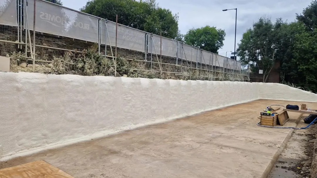 A piled wall sprayed and sealed with closed-cell foam, the layer following the piles and the joints between them.