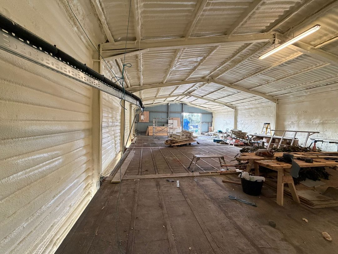 Inside a workshop after treatment: walls and roof sprayed in a continuous cream closed-cell layer, a timber floor and workbenches along the wall.