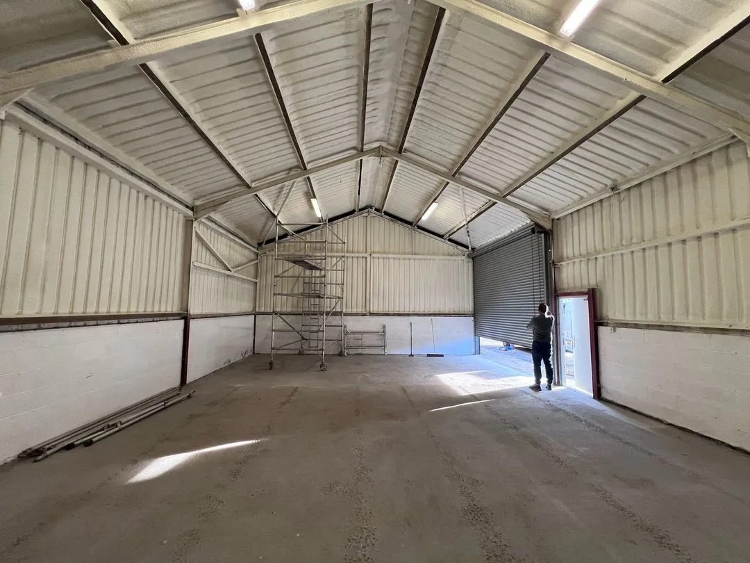 A steel portal-frame workshop interior with a pale lined roof and walls, a roller shutter and a scaffold tower during the works.