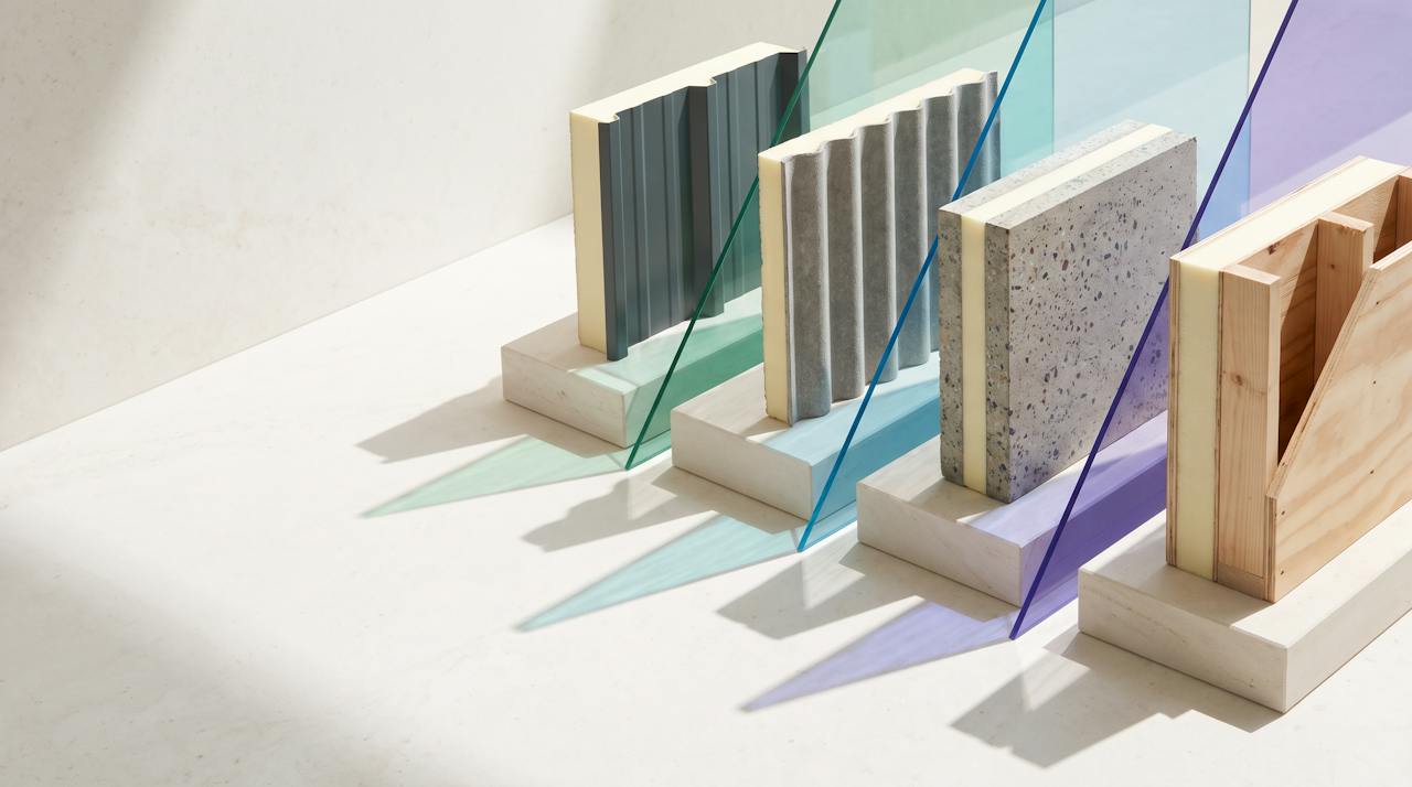A family of cut-section samples on stone plinths: profiled metal, corrugated fibre-cement, a concrete slab and a timber stud, each with a cream closed-cell layer, under hard-edged glass light planes.