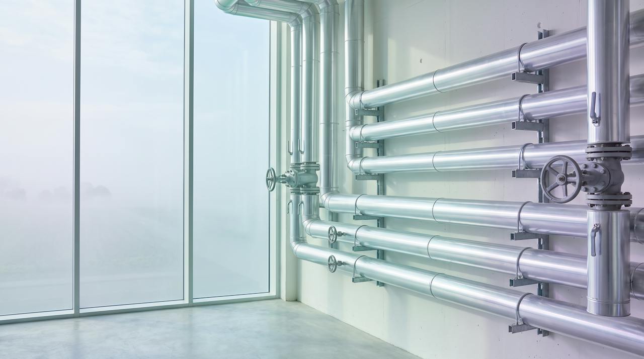 Industrial pipework runs and bends on supports inside a plant building.