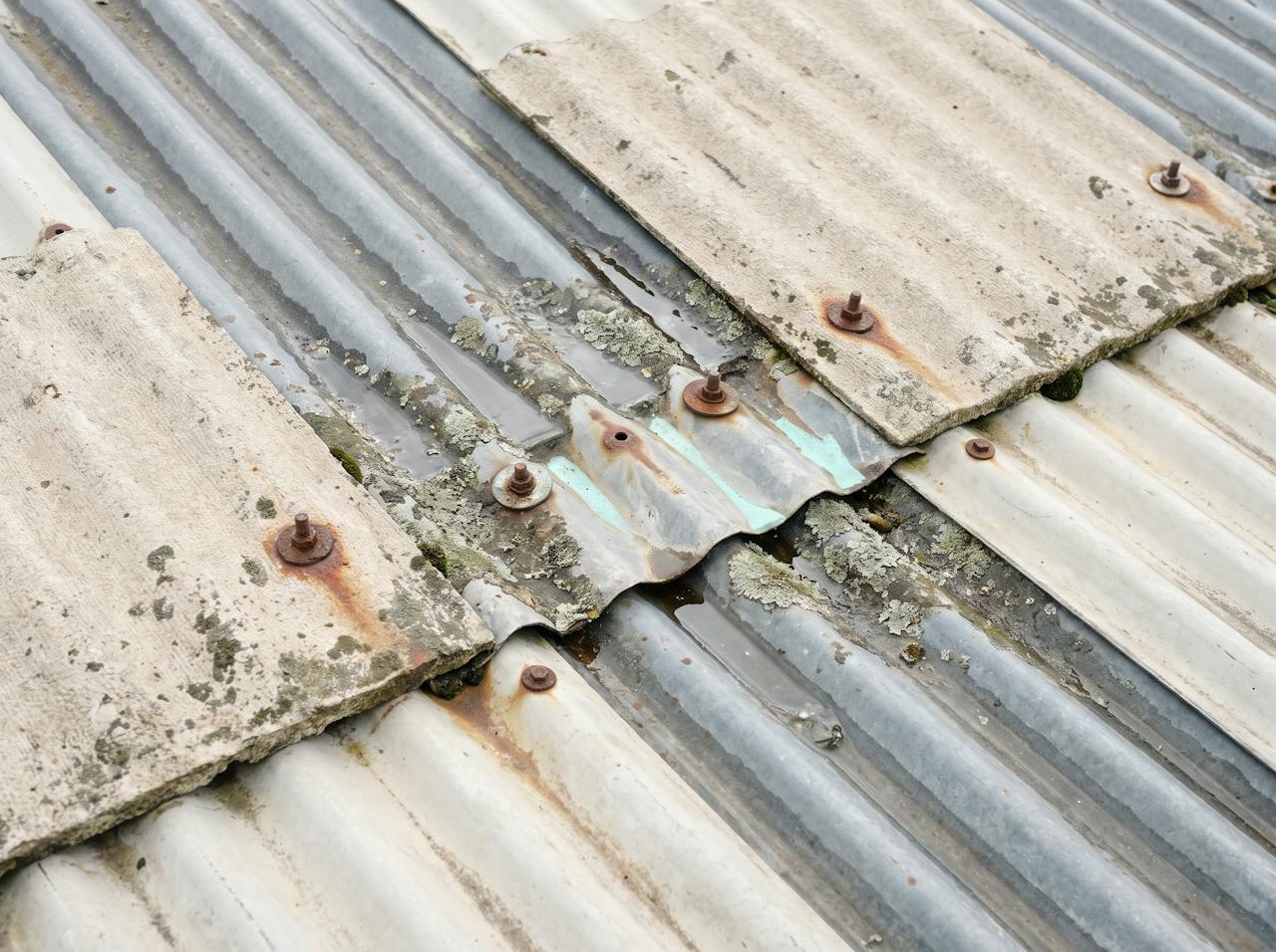 A close detail of a weathered corrugated asbestos-cement roof from above: grey porous sheet, moss in the troughs, a rusted hook bolt and a hairline crack running from it.