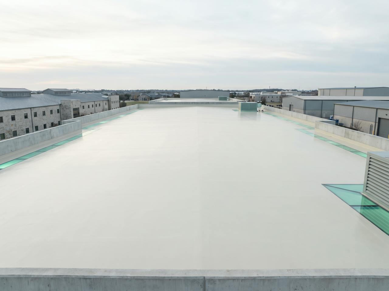 A corrugated asbestos-cement roof from above finished in a smooth, pale silicone coating, every fixing capped and every lap sealed, rainwater beading and running off under a bright sky.