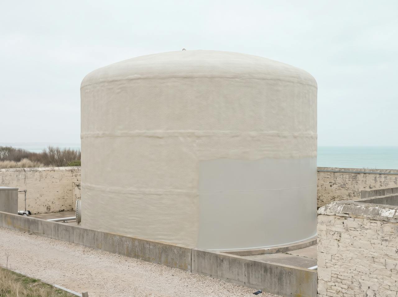 A vertical storage tank with a smooth, continuous cream closed-cell jacket finished in a pale protective coating, cut back neatly around a flanged nozzle and the legs.
