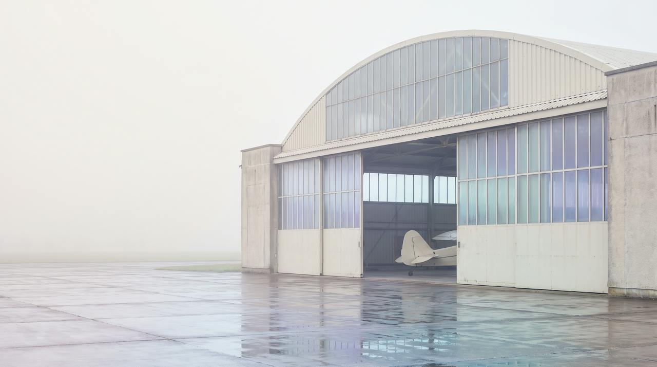 The interior of a large aircraft hangar, arched roof and open doors, pale light.