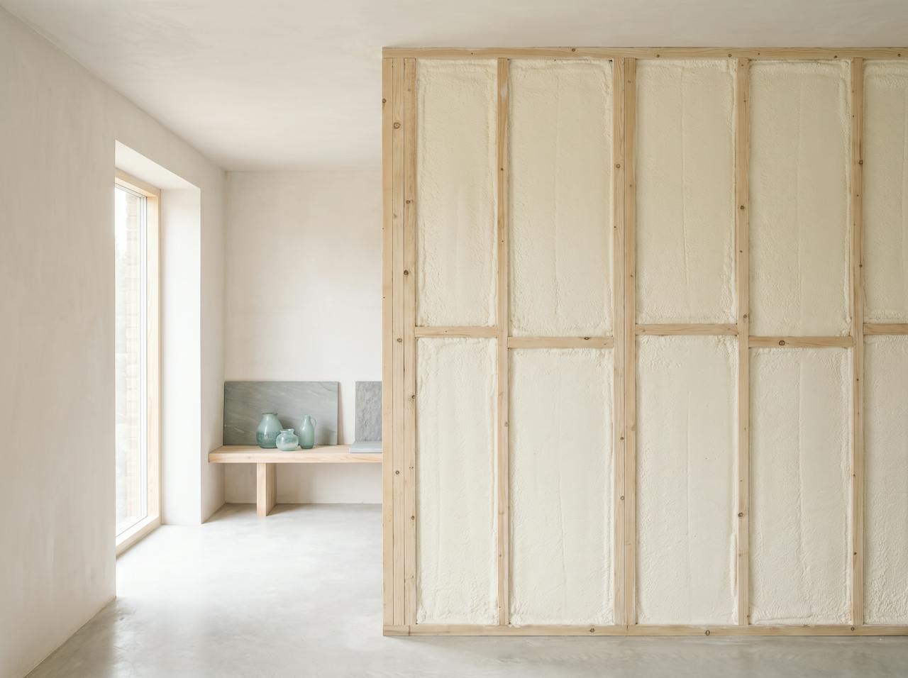 The inside of a metal-clad wall with a continuous cream closed-cell layer following the profile between the rails, the rails enclosed, even daylight along the wall.