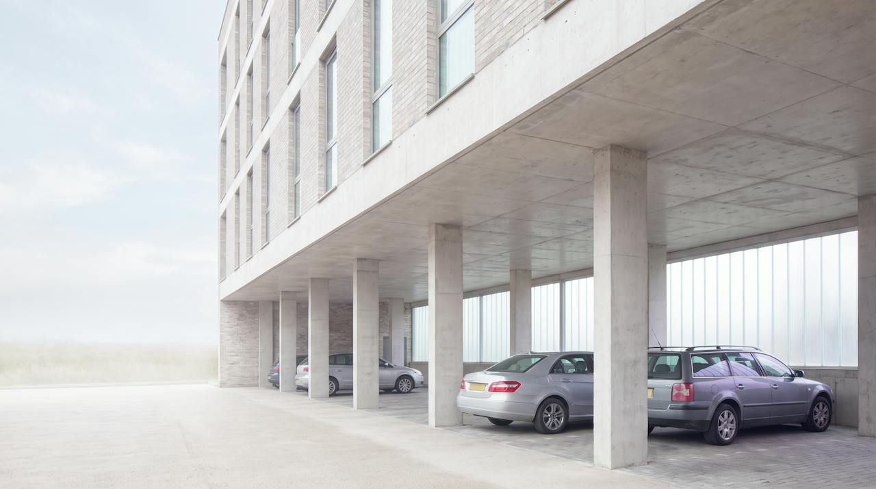 A concrete undercroft car park with downstand beams and a row of columns, daylight from the open side.
