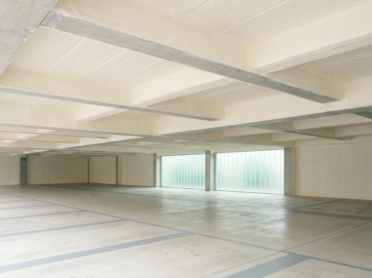 The same soffit after treatment: a continuous cream closed-cell layer with a pale coating wrapping the slab and downstand beams, columns left clear.