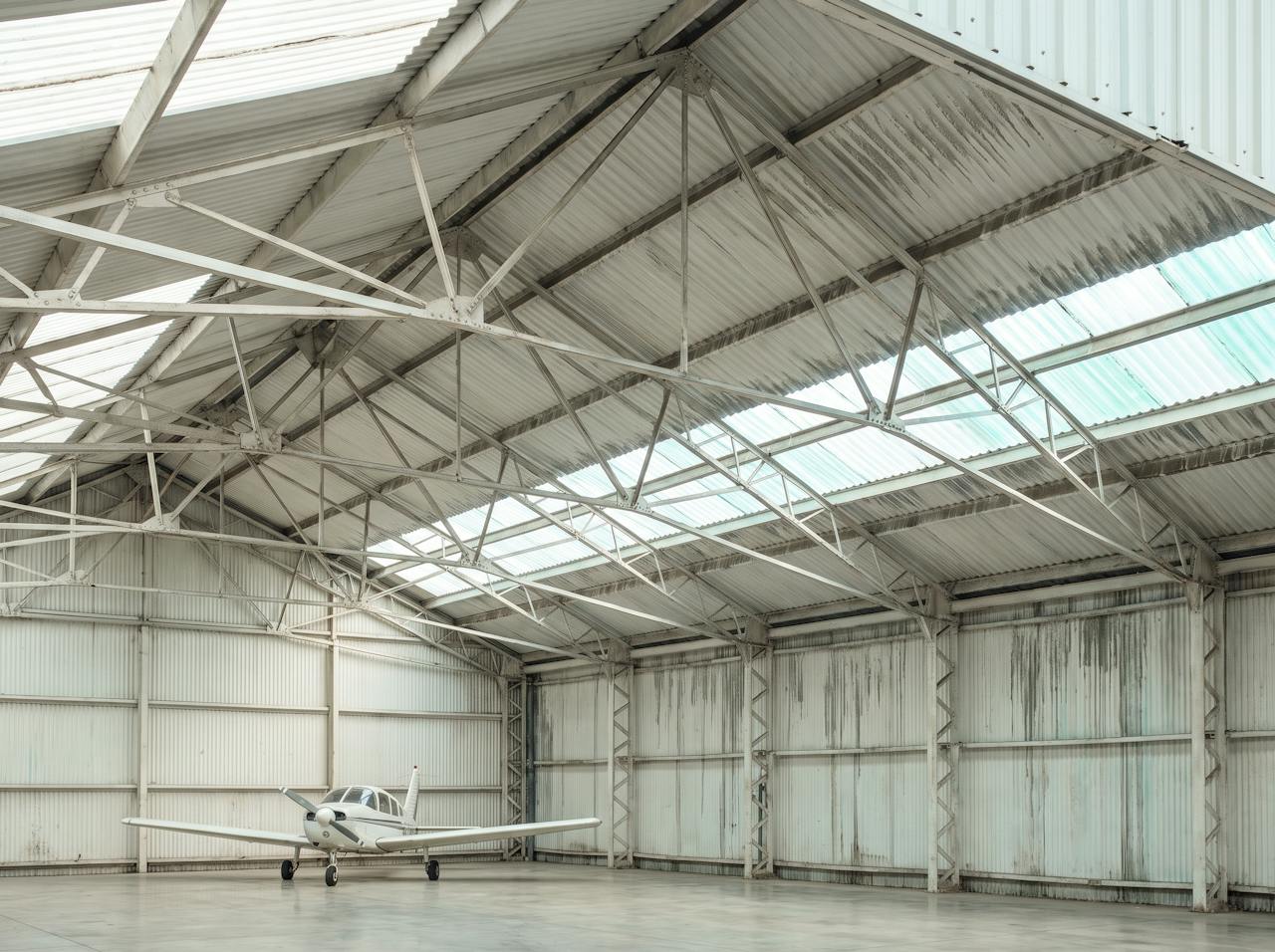 Looking up inside an unheated hangar on a cold morning: fine condensation across the underside of the profiled steel roof between the trusses, a drip line forming under a valley.