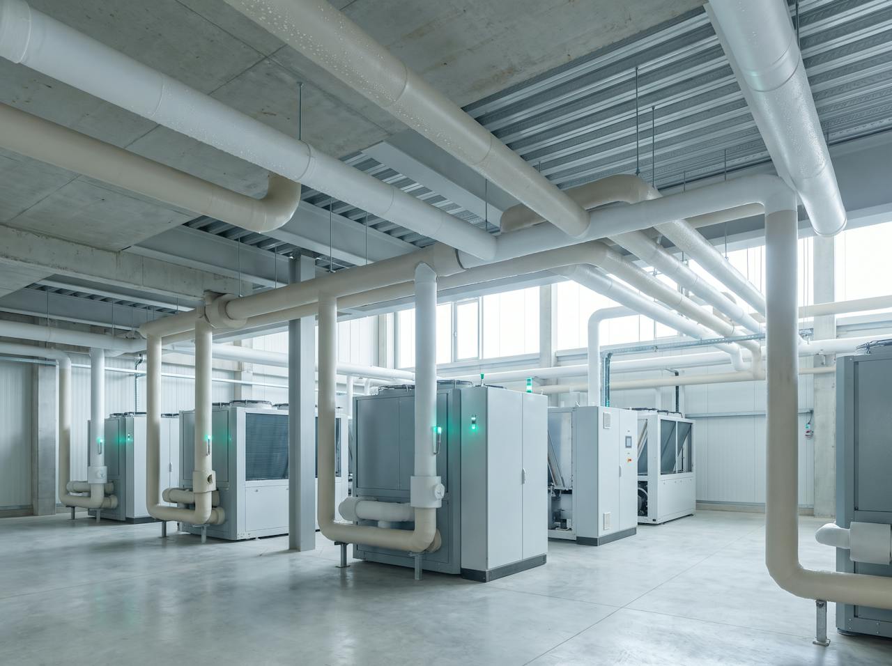 Inside the roof void above a data hall: a bare profiled steel roof and purlins above cable containment and ductwork, condensation beaded along a purlin flange, a drip tray fixed beneath it.