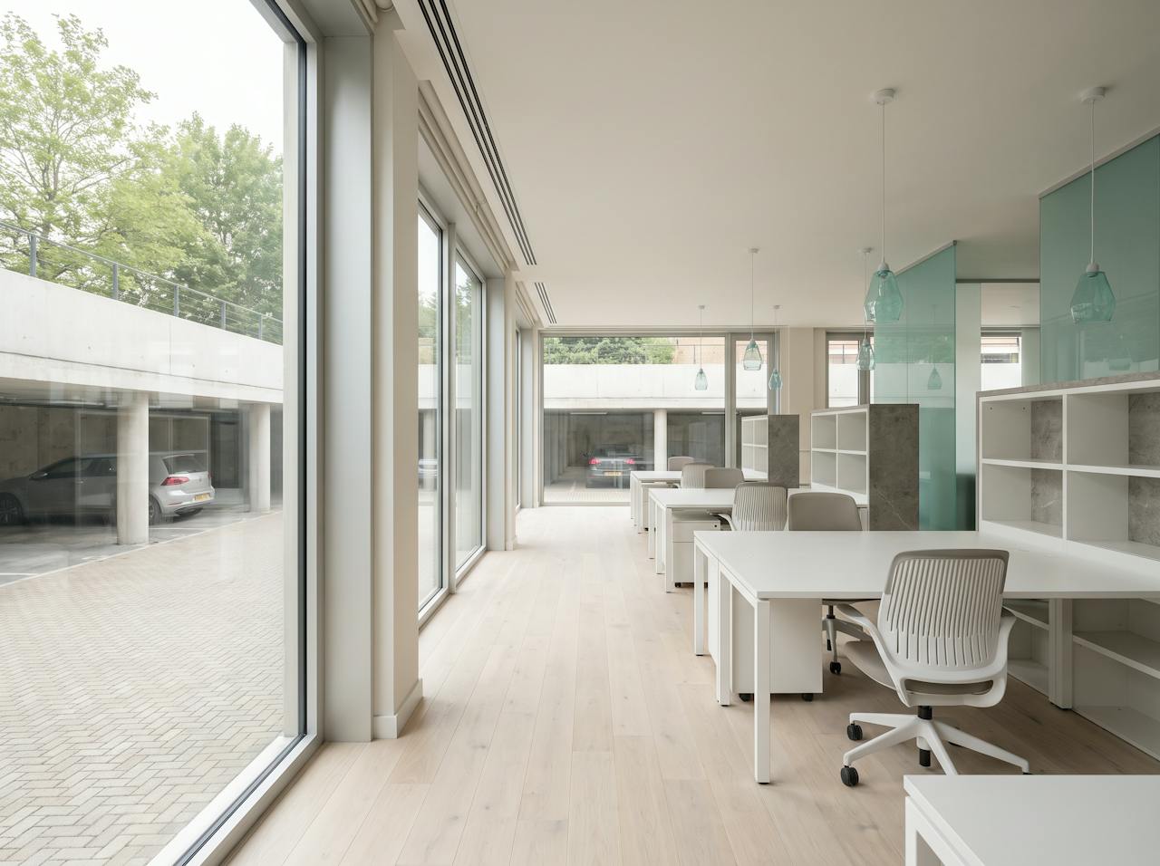 An open-plan office on the ground floor of a commercial building, the desks nearest the window sitting over the open car park below, pale morning light across a cold floor.