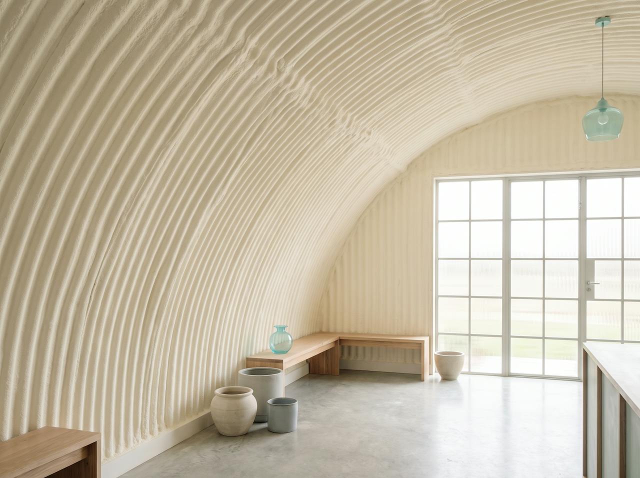 Inside a Nissen hut after treatment: the whole arch lined in a continuous cream closed-cell layer that follows every corrugation, the curve intact.