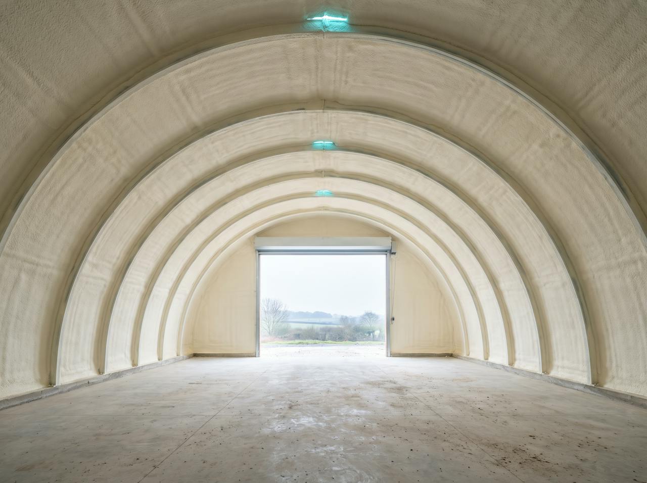 Inside an arch-frame building after treatment: walls and crown lined in one continuous cream closed-cell layer, the corrugations still reading through the curve.